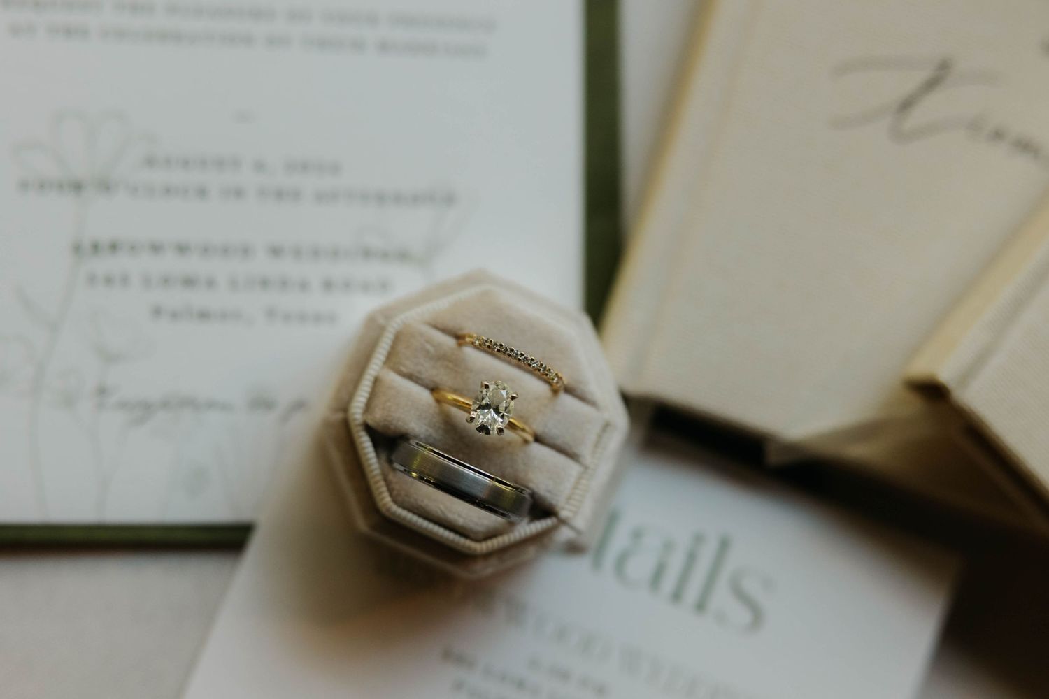 Wedding rings and gold bracelet displayed in velvet box beside elegant wedding invitation suite.