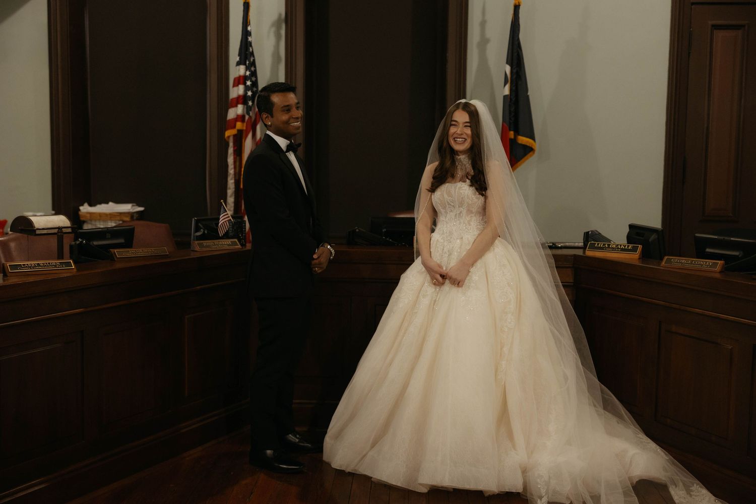 Bride in ballgown and groom in tuxedo standing in elegant courthouse for intimate wedding.