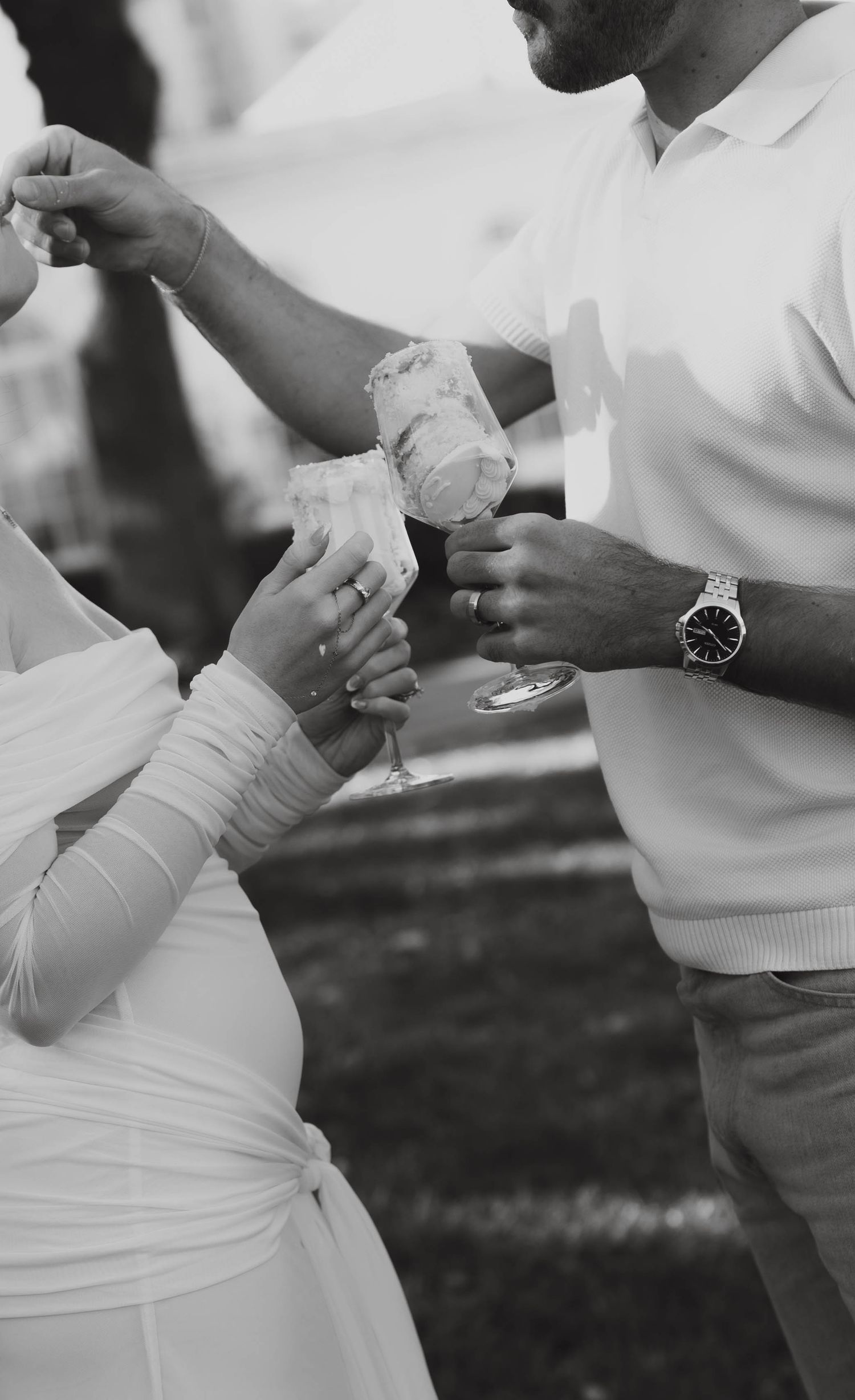 Black and white photo of couple toasting with floral cocktails at outdoor wedding celebration.