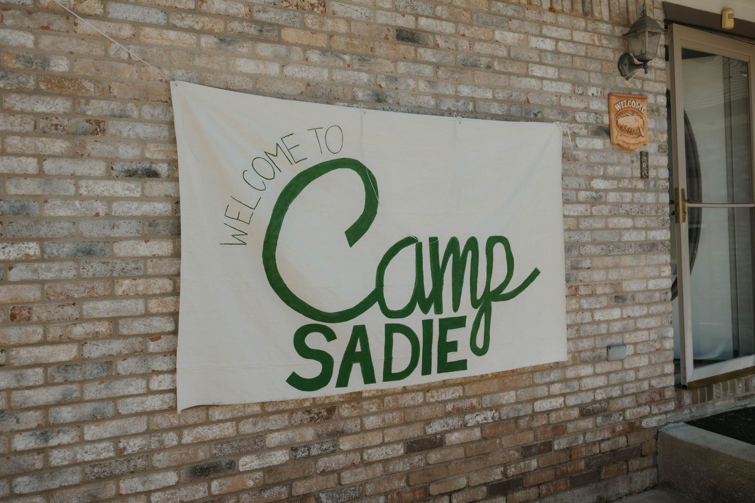 Welcome to Camp Sadie banner on brick wall at wedding venue entrance.