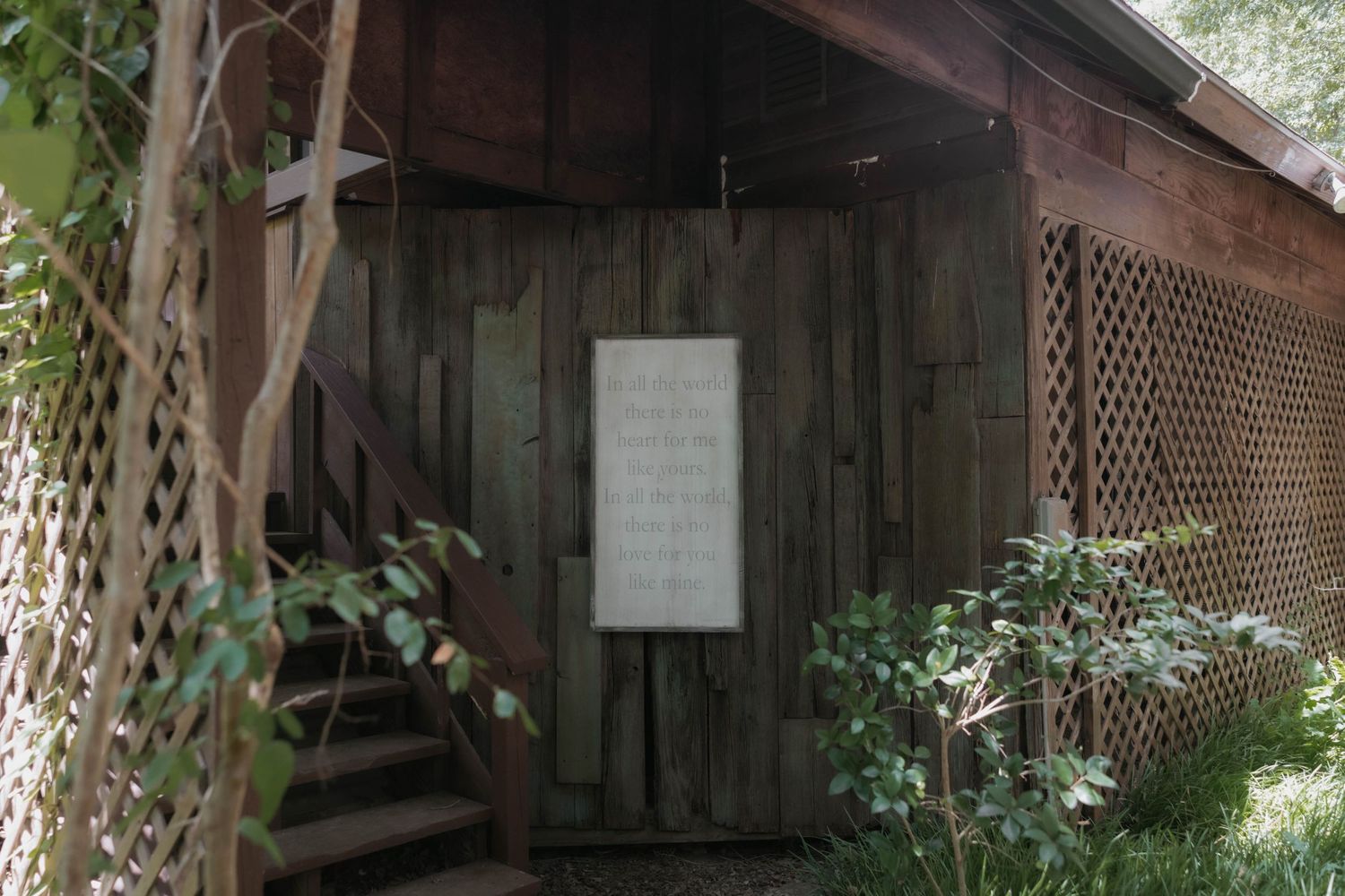 Rustic wooden wedding venue entrance with white sign surrounded by lush green foliage and lattice.