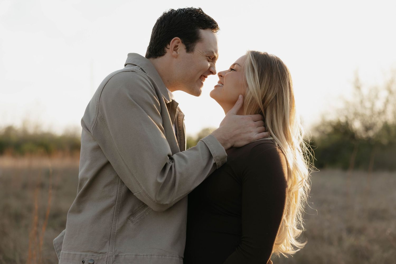 Romantic couple embracing and touching foreheads in golden hour light in a field.