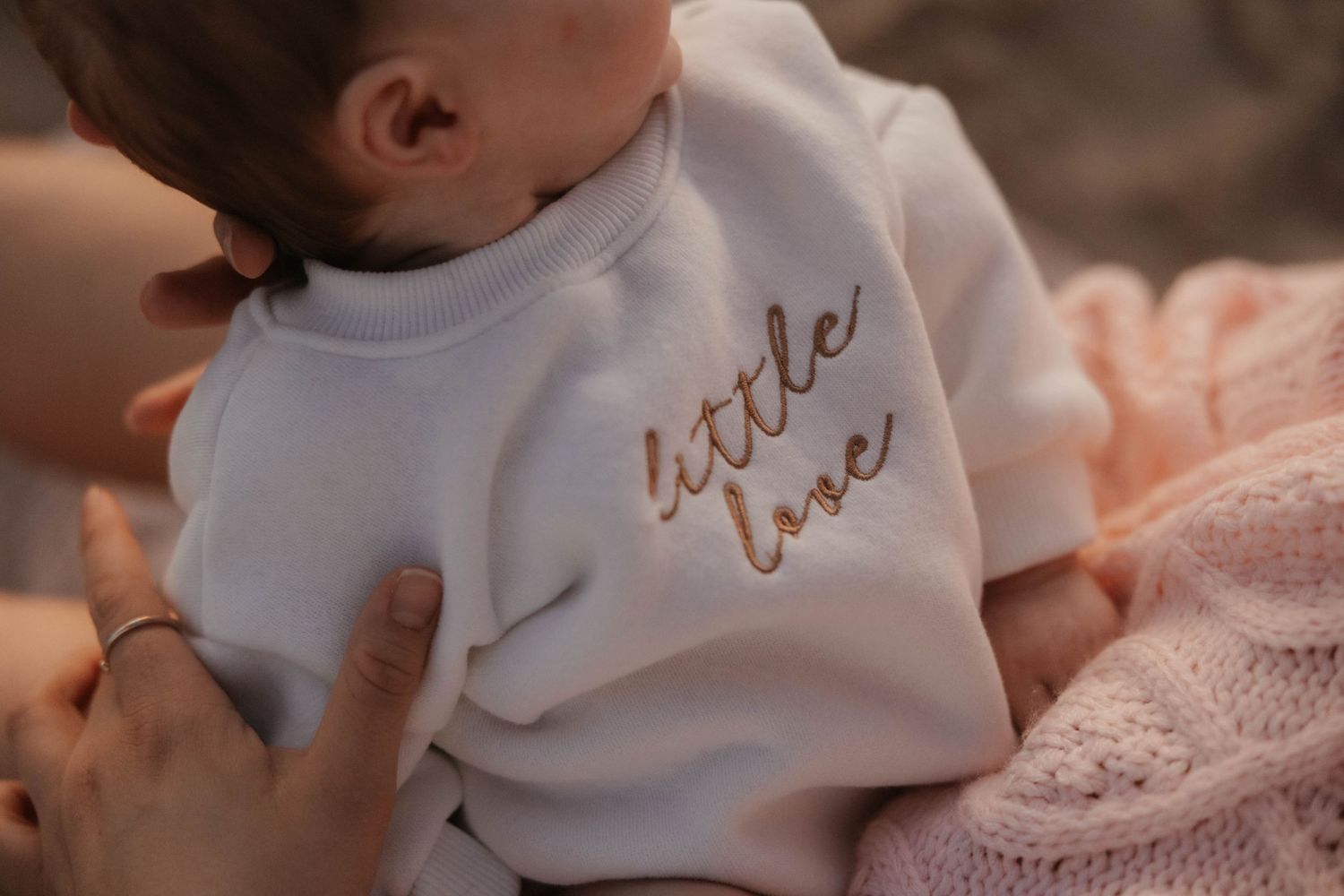 Close-up of newborn baby in white embroidered little love sweatshirt being held gently.