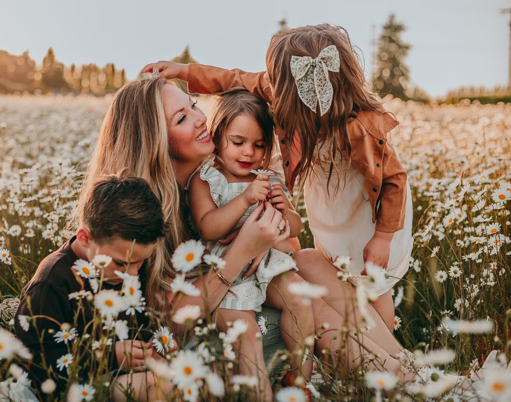 A family shares tender moments together in a golden field of blooming daisies at sunset.