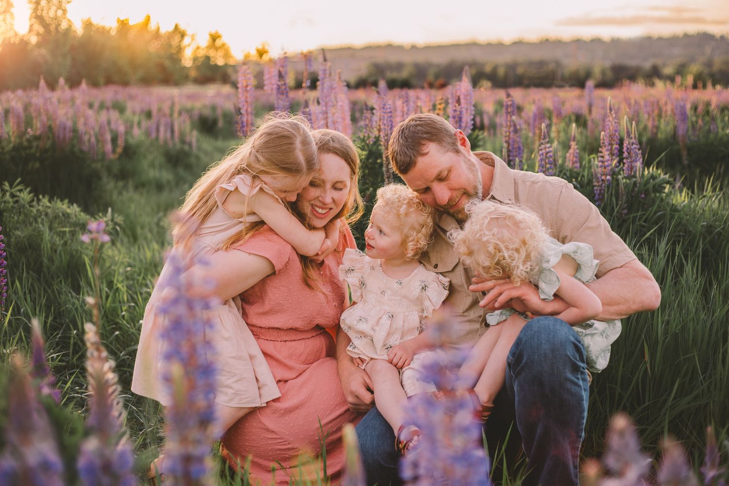 A family enjoys a sunset photo session in a field of purple lupine flowers during golden hour during their Seattle wildflower family photos