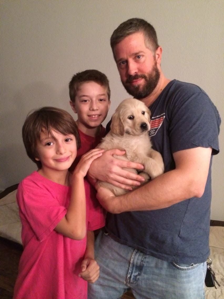 A man and two boys smile while holding an adorable golden retriever puppy indoors.