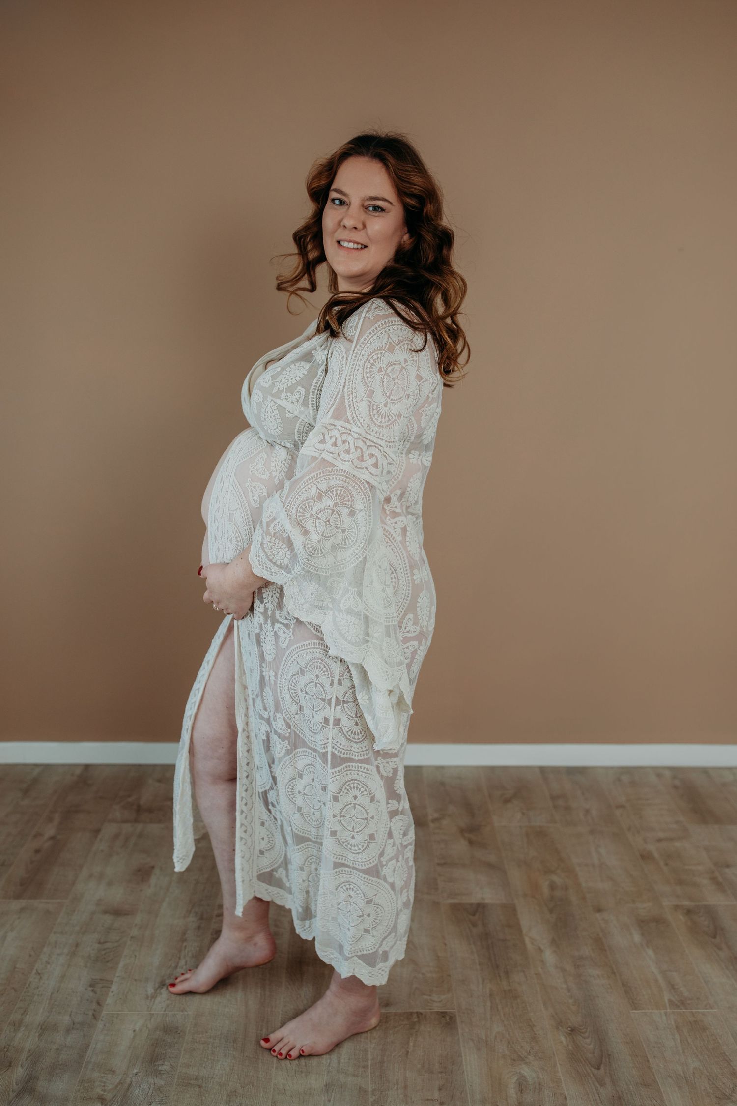 Zwangere vrouw in kimono. Handen op de buik en ze kijkt lachend naar de camera.
