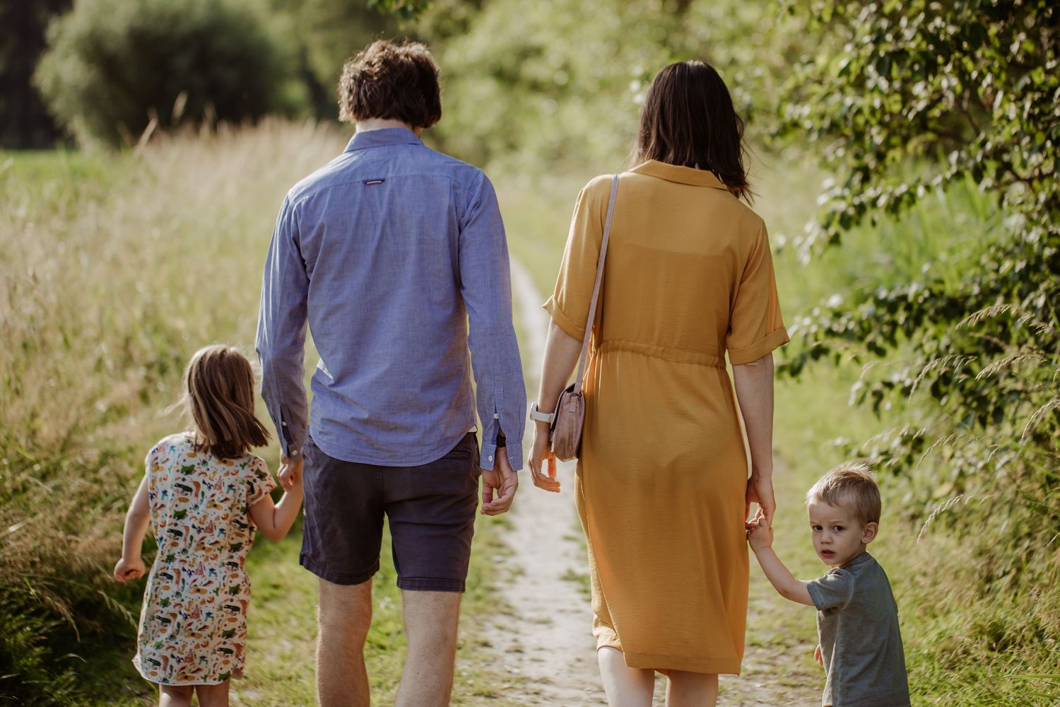 Een familie (mama, papa, dochter en zoon) aan het wandelen. Ze wandelen hand in hand. De zoon kijkt achterom naar de fotografe.