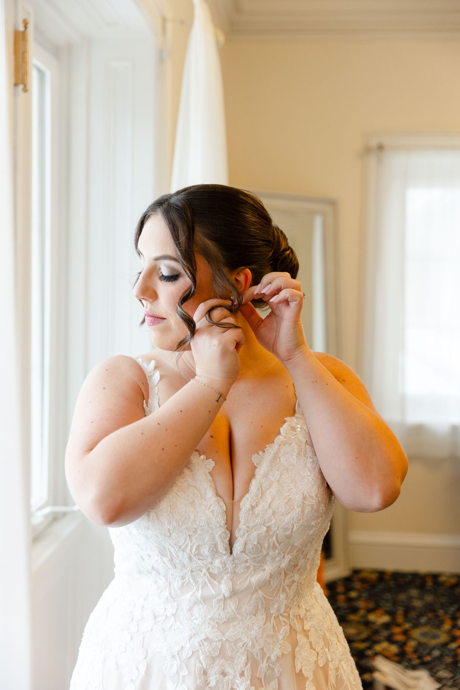 Bride getting ready, adjusting earrings, looking down with glam makeup Tupper Manor in Beverly, MA