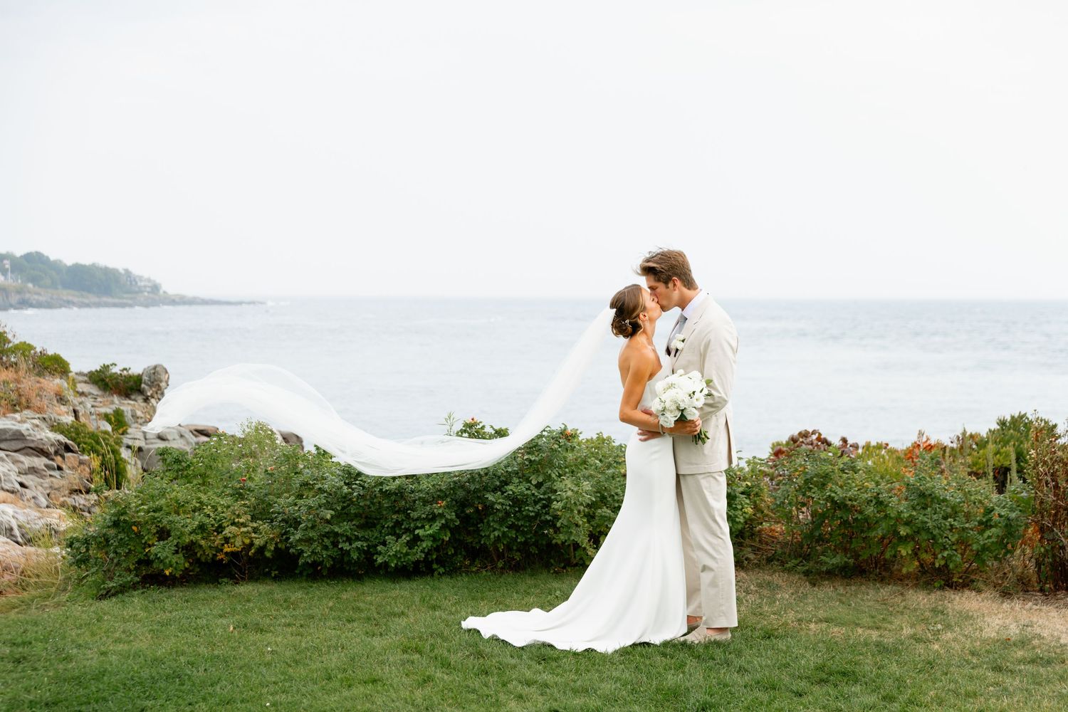 Bride and groom portrait kissing with veil blowing in the wind with ocean view and cliffs at Stage Neck Inn in York Harbor, Maine