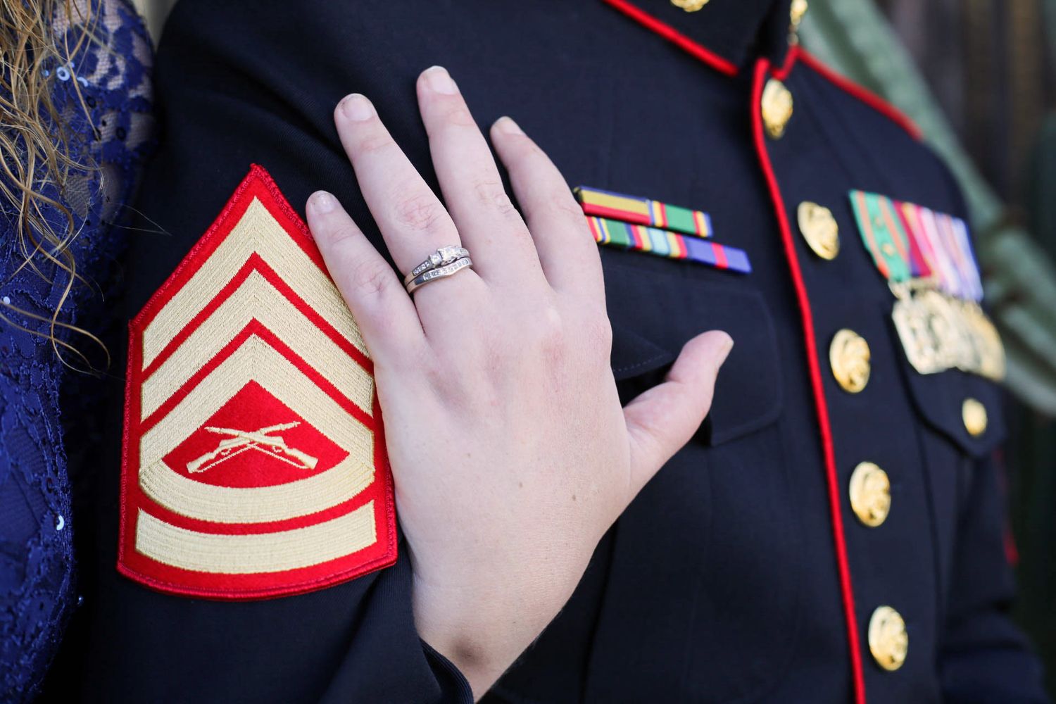 Close-up of engagement ring on woman's hand resting on Marine Corps dress blue uniform with sergeant rank.