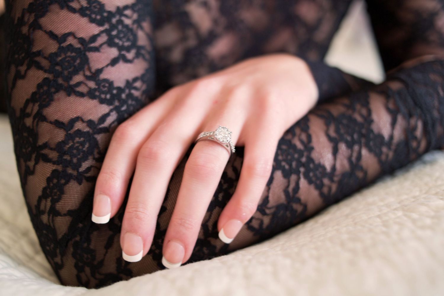 Close-up of a woman's hand wearing a diamond engagement ring on black lace fabric.