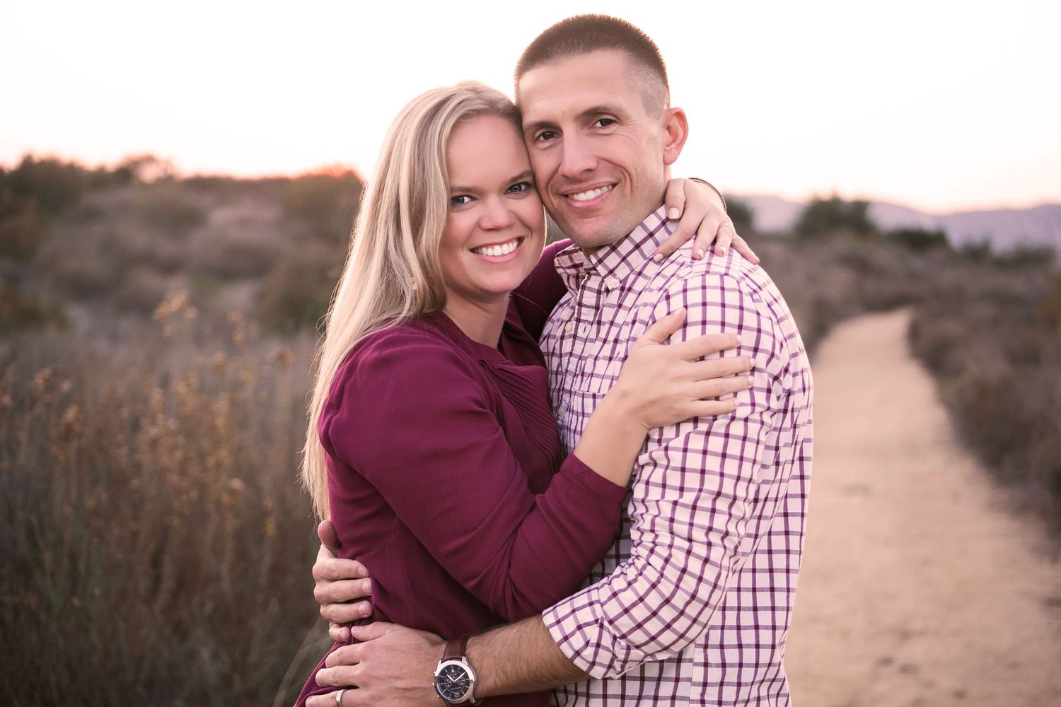 Smiling couple embracing at golden hour on scenic outdoor path for couples portrait session.