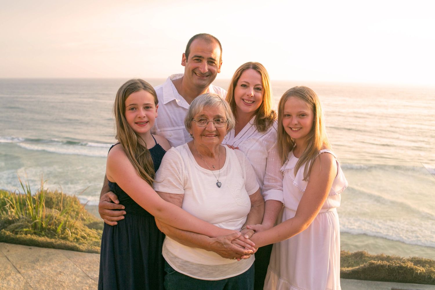 Extended family of eight dressed in black posing together on a sandy beach at sunset.