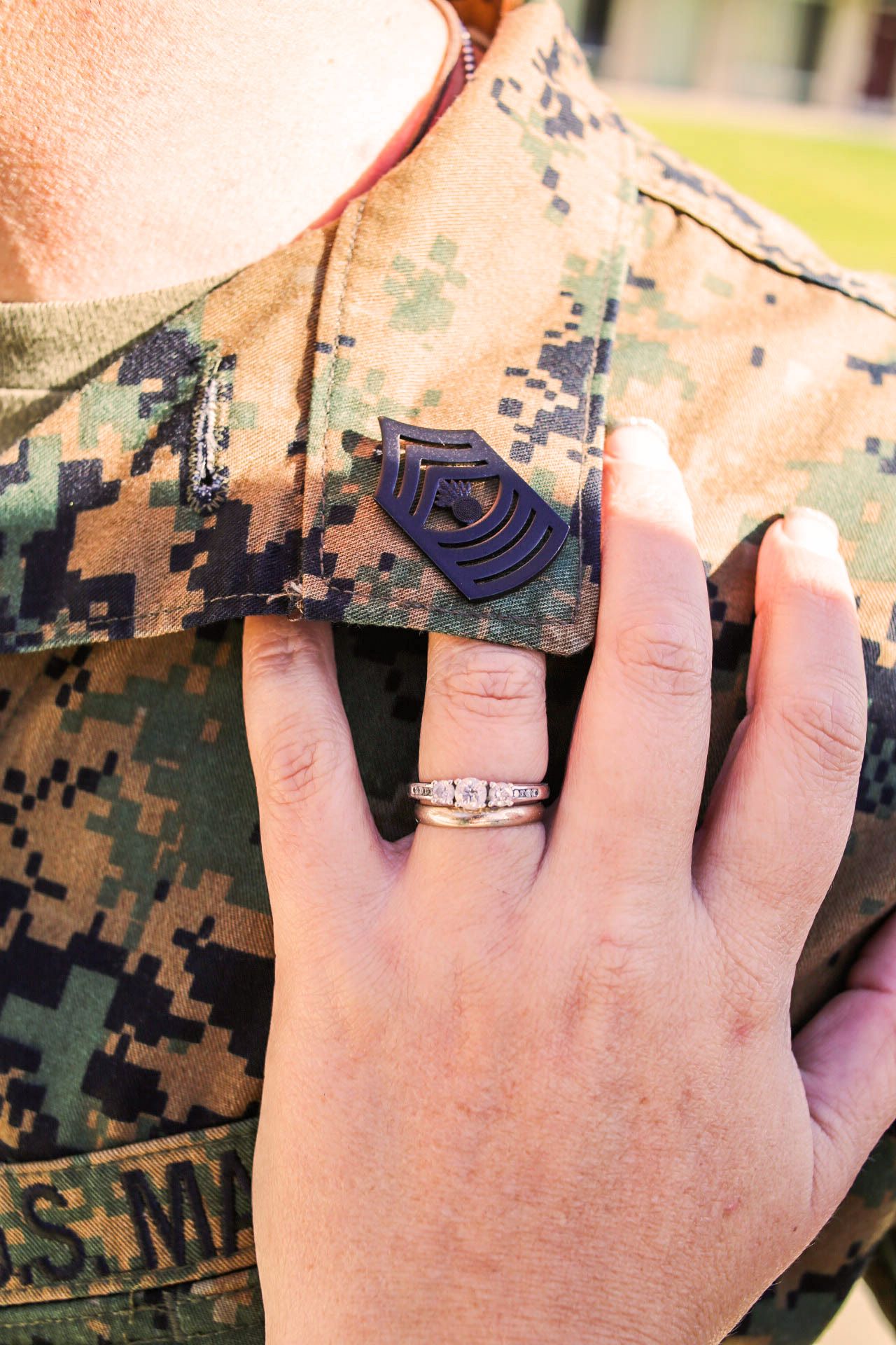 Engagement ring on woman's hand resting on Marine Corps camouflage uniform with staff sergeant insignia.