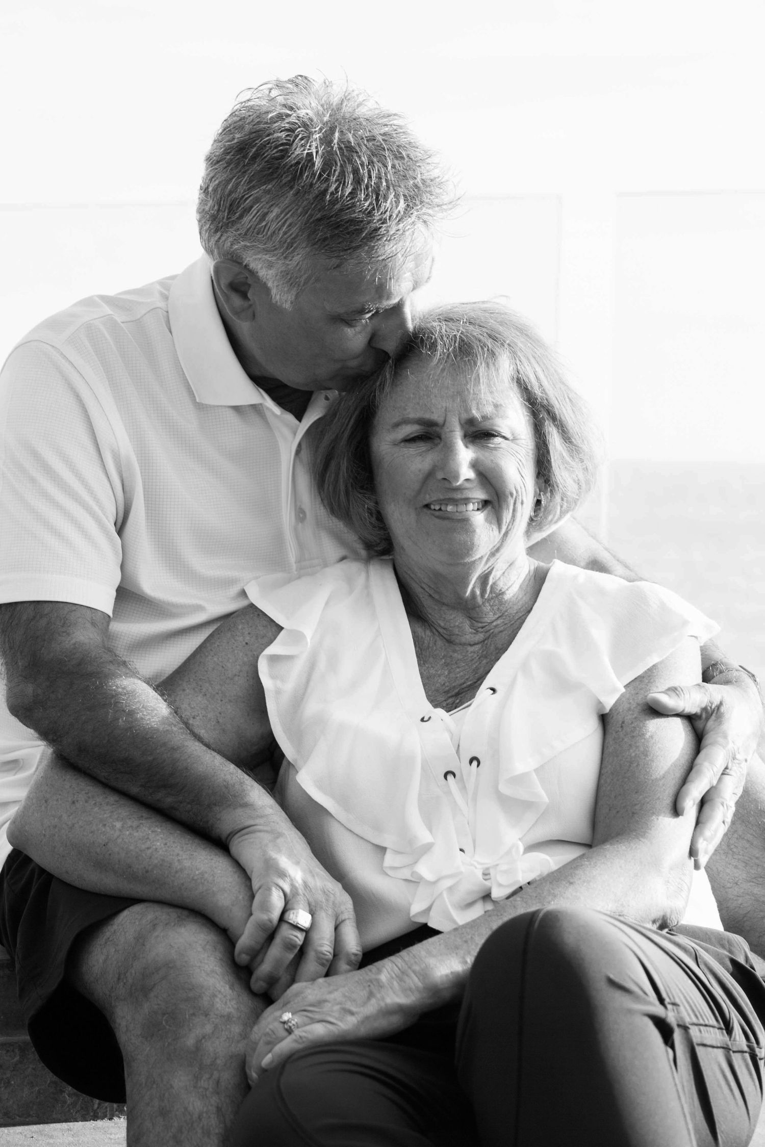 Black and white portrait of mature couple sharing tender moment, man kissing womans head.