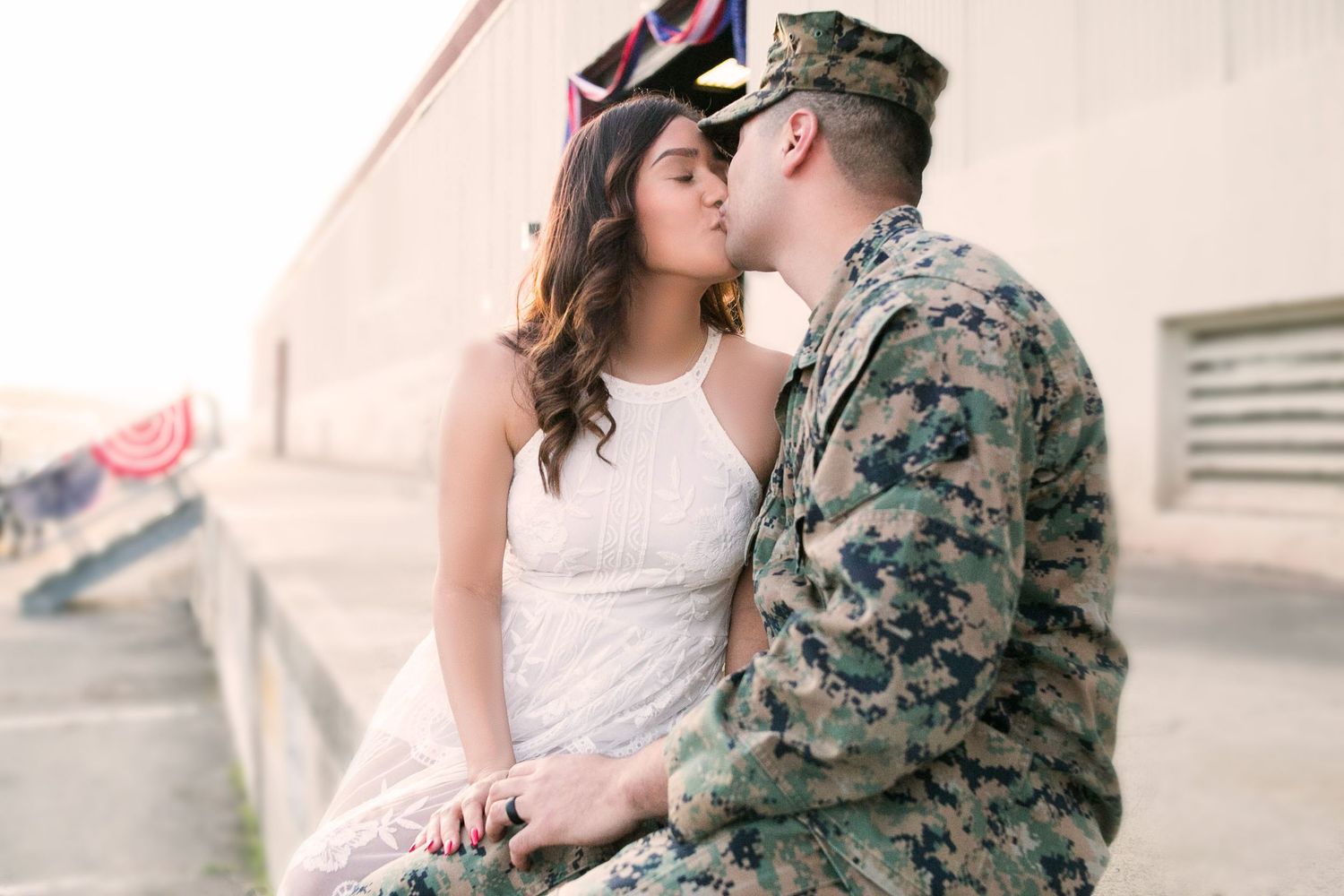 Woman in white dress kissing man in military uniform during couples portrait photography session.
