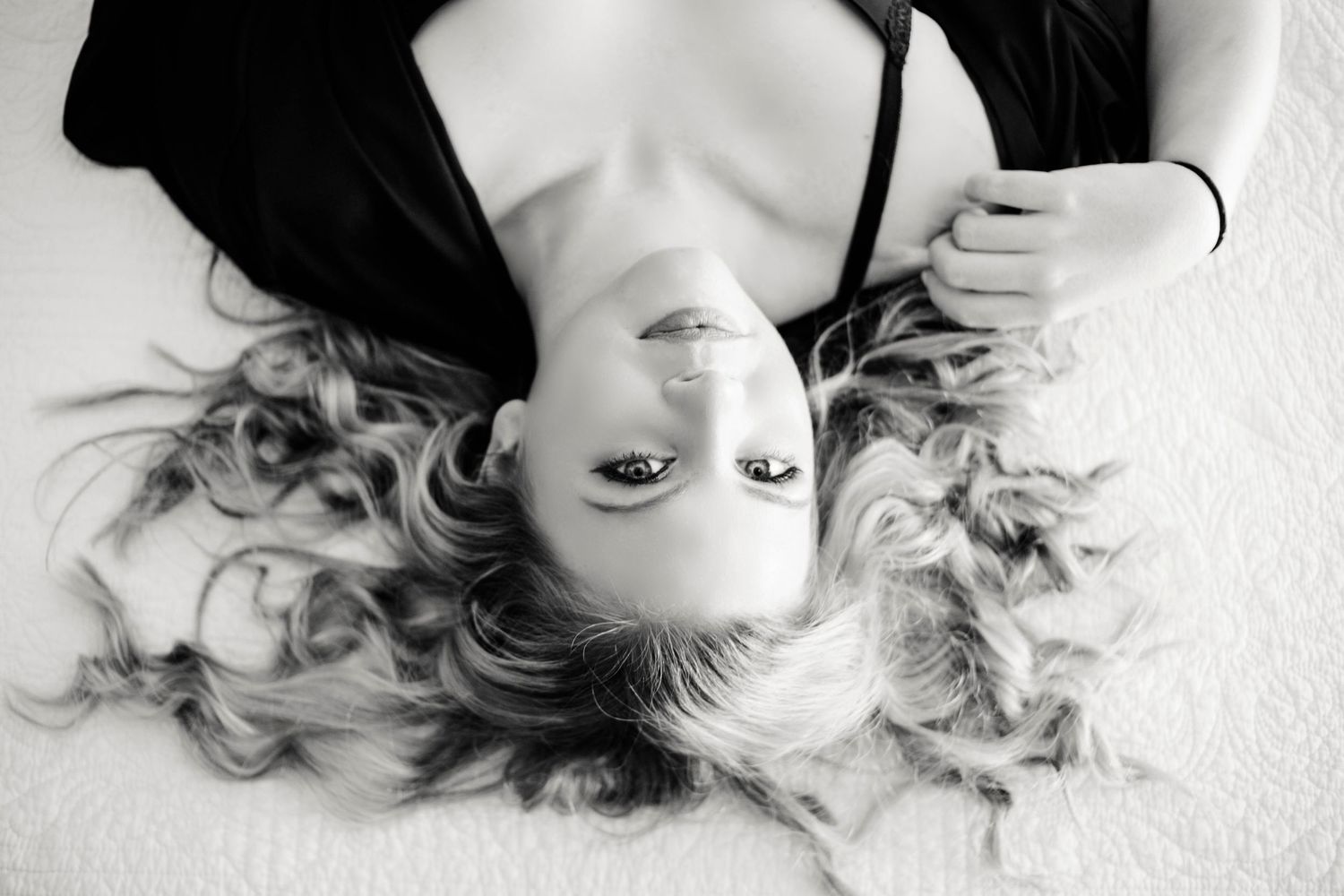 Black and white portrait of a woman with long curly hair lying down looking up at the camera.