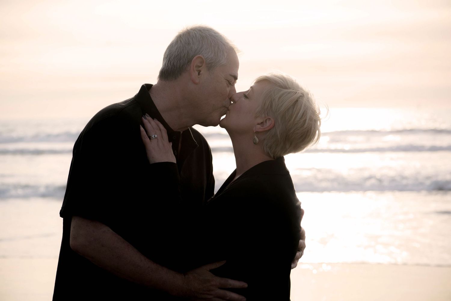 Romantic couple silhouetted kissing on beach at sunset during couples portrait photography session.