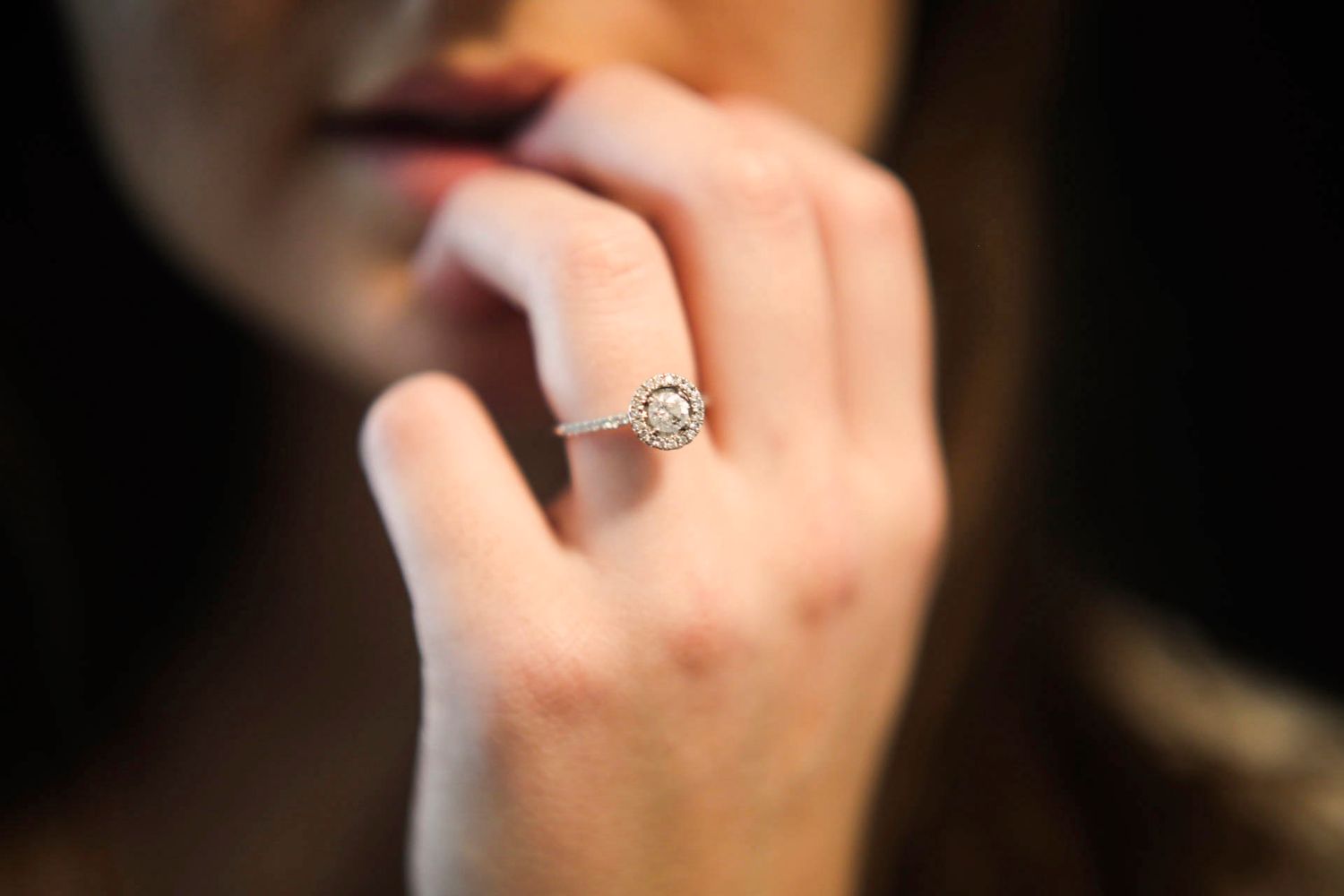 Close-up of woman's hand featuring elegant halo diamond engagement ring with pave band.