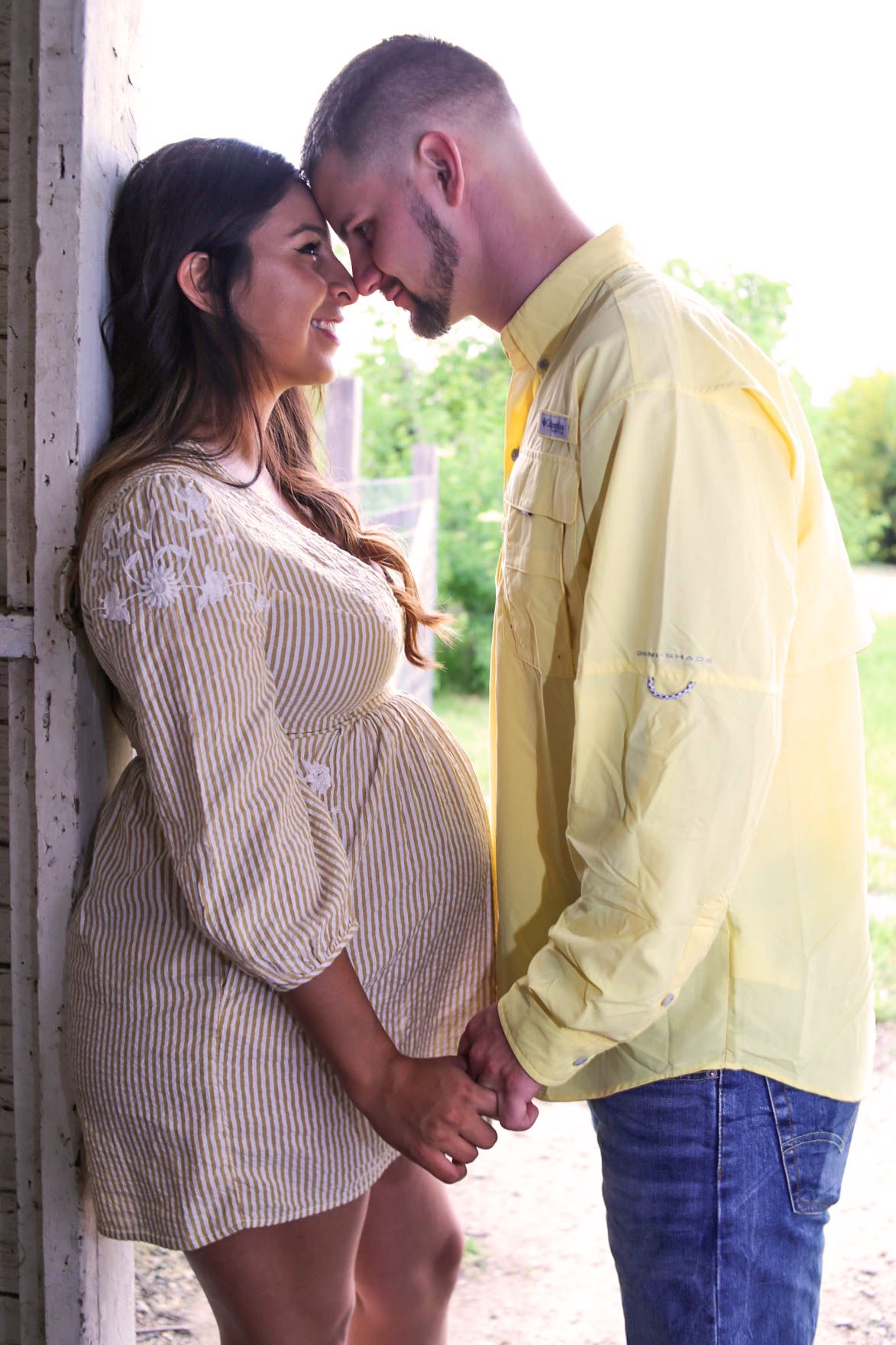 Expecting couple holds hands and touches foreheads tenderly during outdoor maternity photo session.