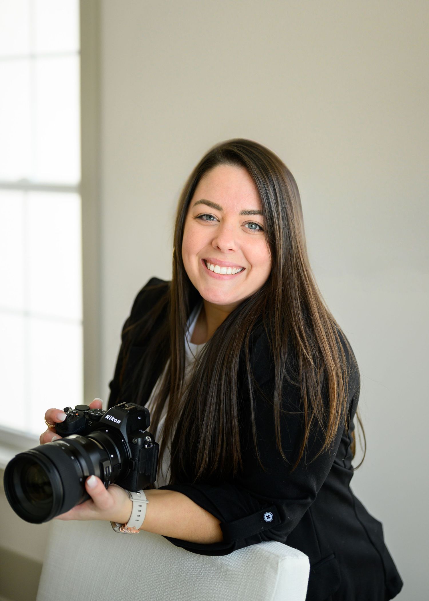 A series of four professional headshots showing a photographer in a black sweater holding a camera against a white background.