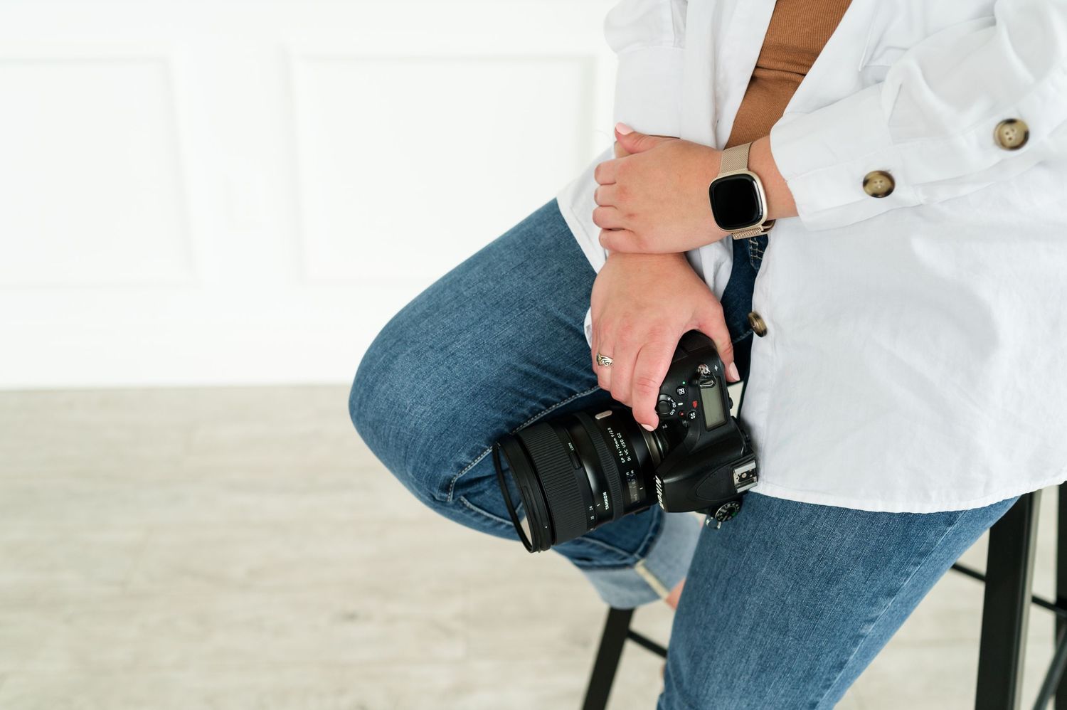 Person in white shirt and jeans sitting on a wooden chair in a bright studio setting.