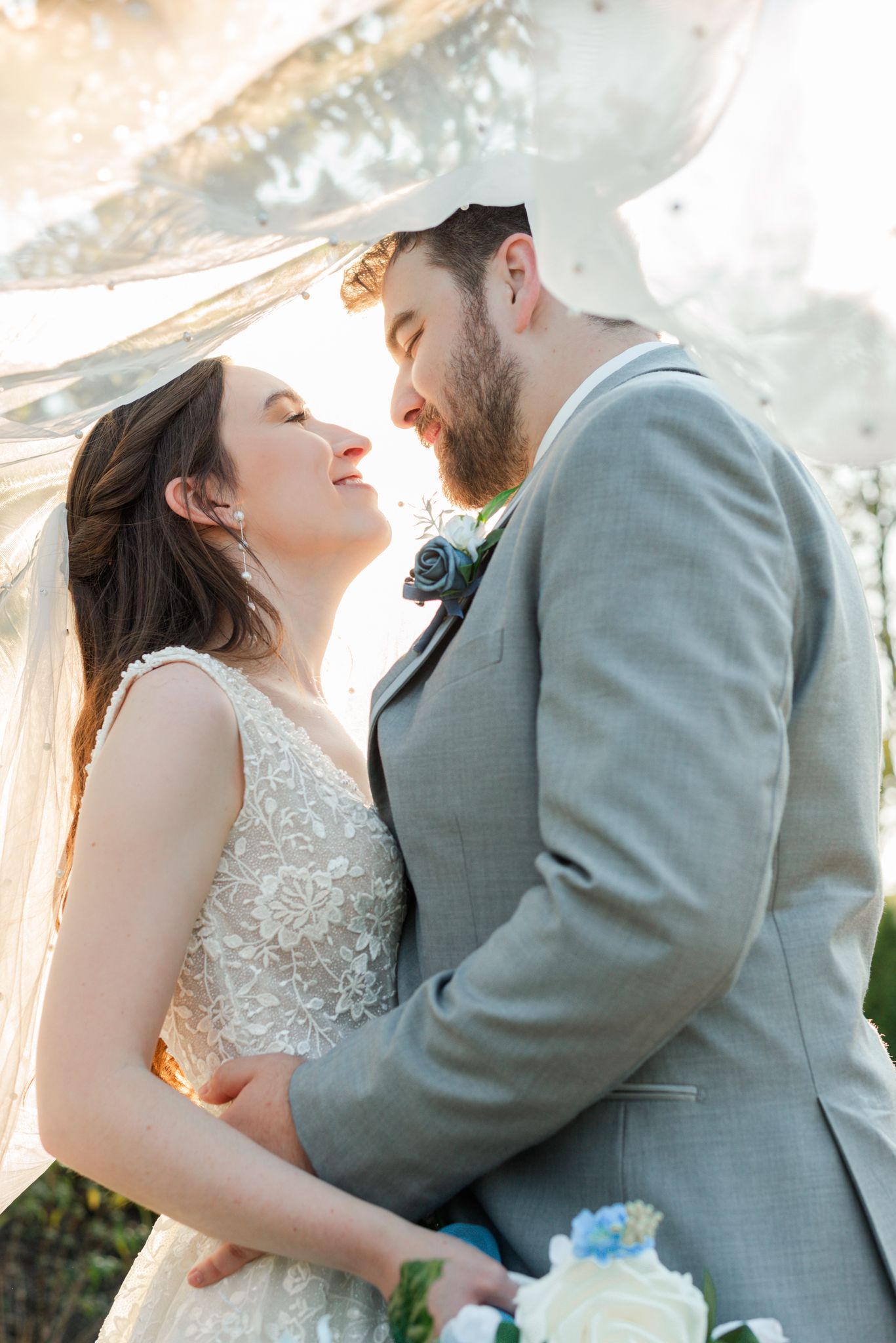 Romantic wedding couple share an intimate moment under flowing veil during golden hour sunset.