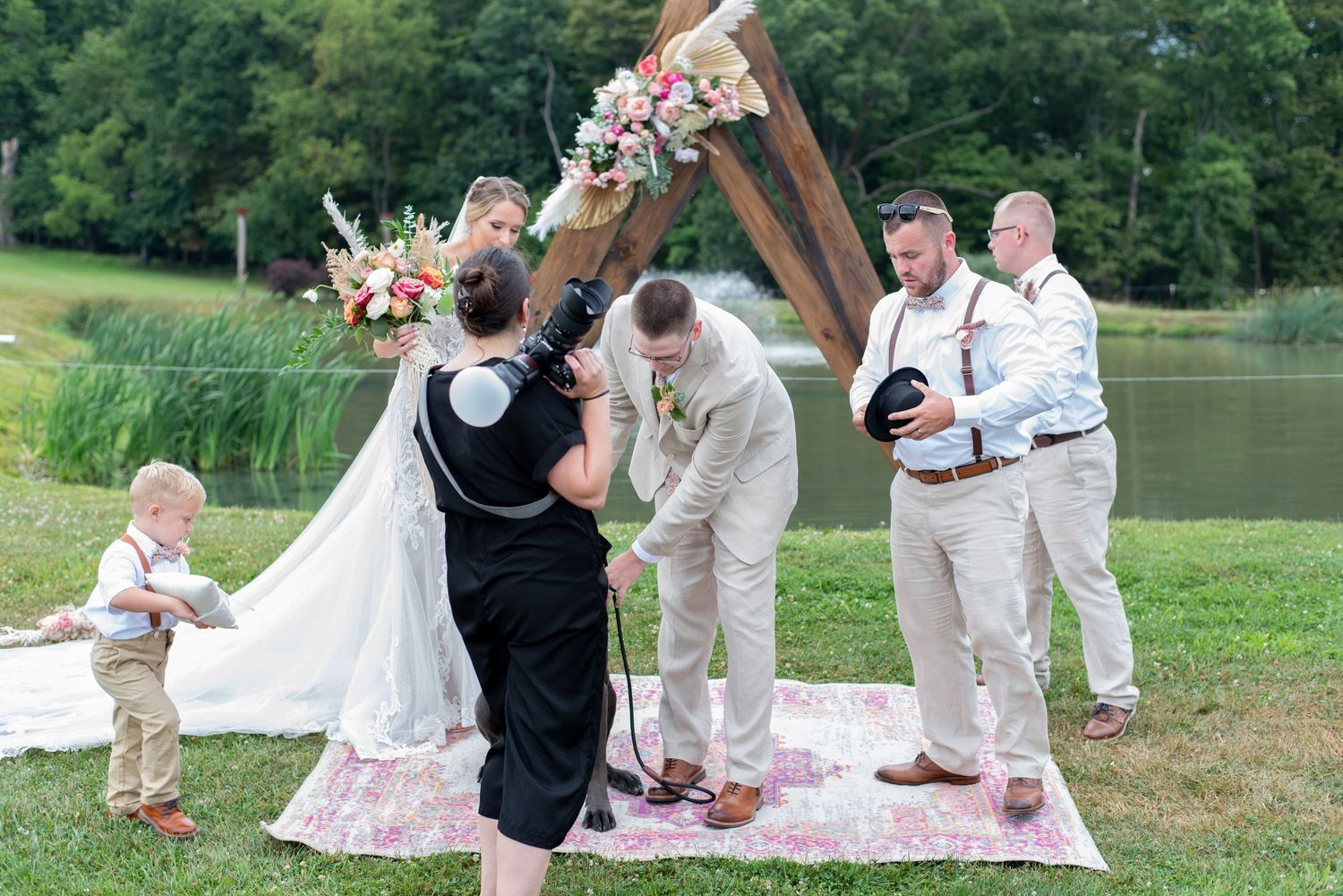 Outdoor wedding party enjoying a picturesque picnic celebration on a grassy hillside near a lake.