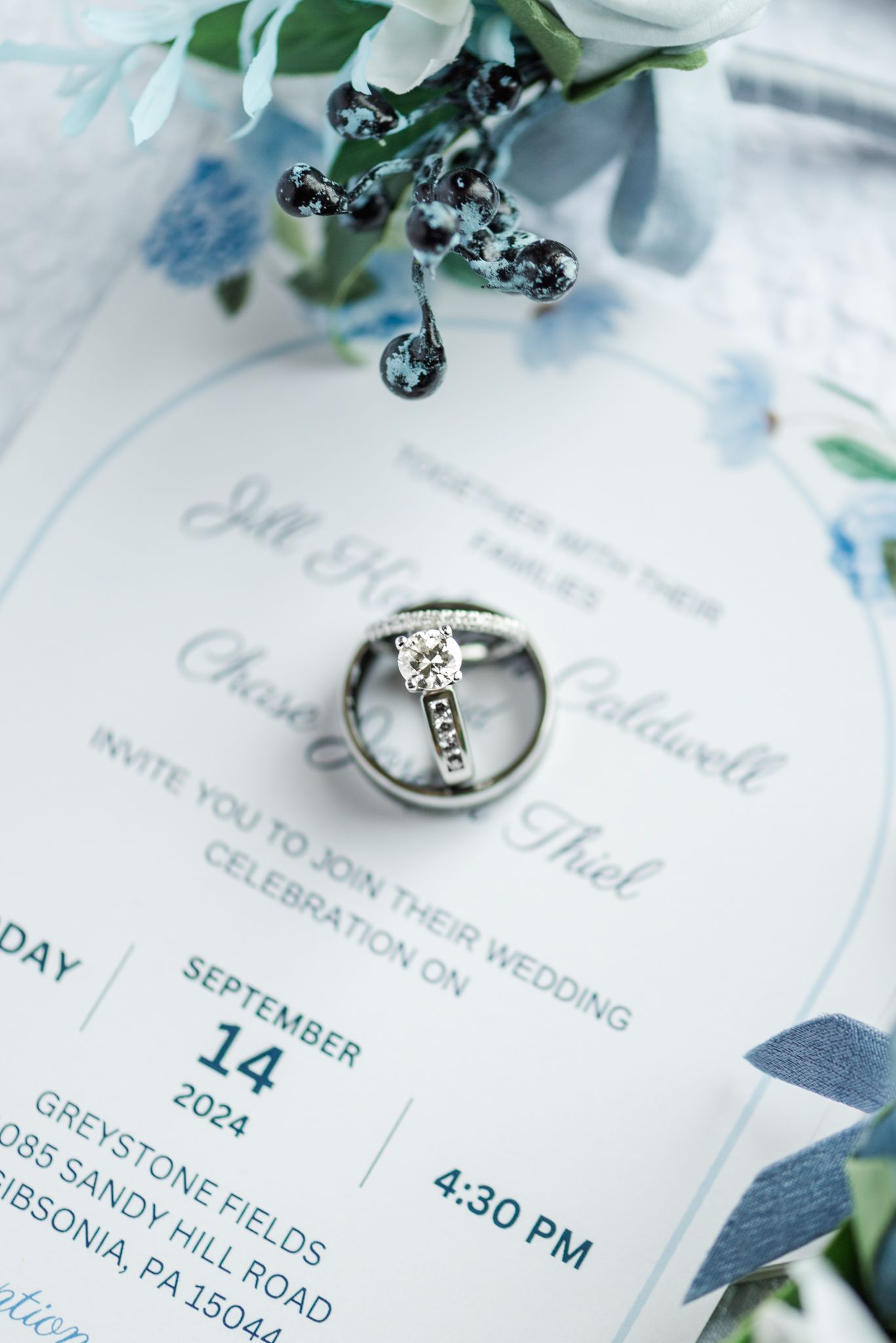 Wedding invitation details showing date, time and venue with an elegant diamond engagement ring and delicate blue florals.
