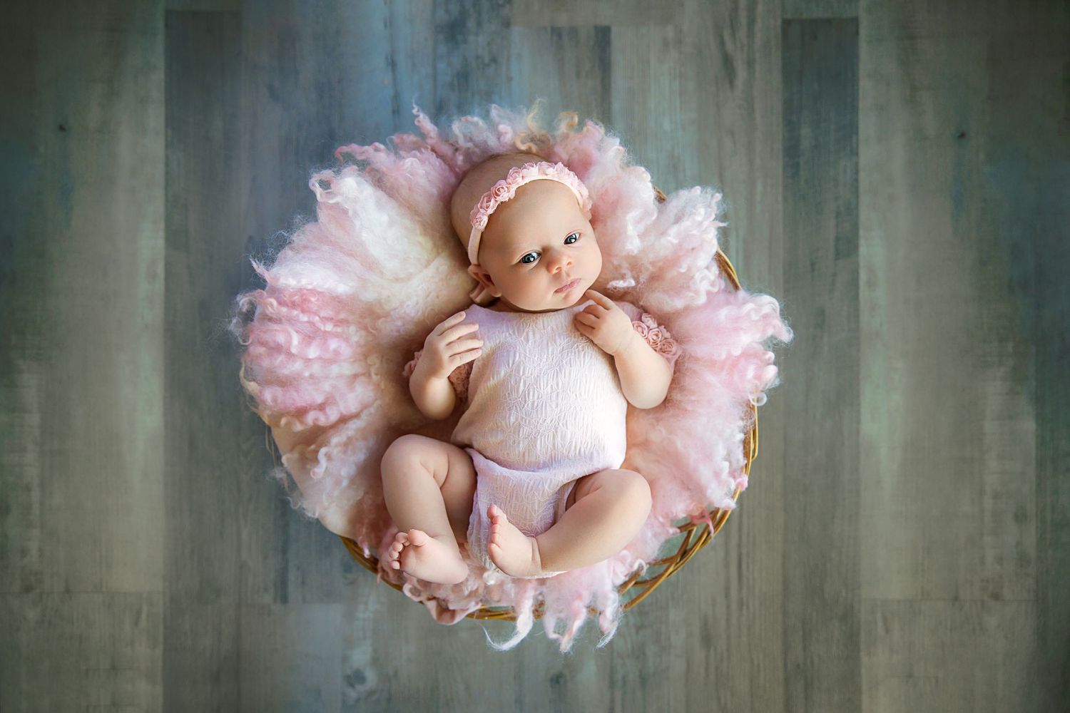 Newborn baby wearing white outfit lies in pink tulle nest against grey backdrop.