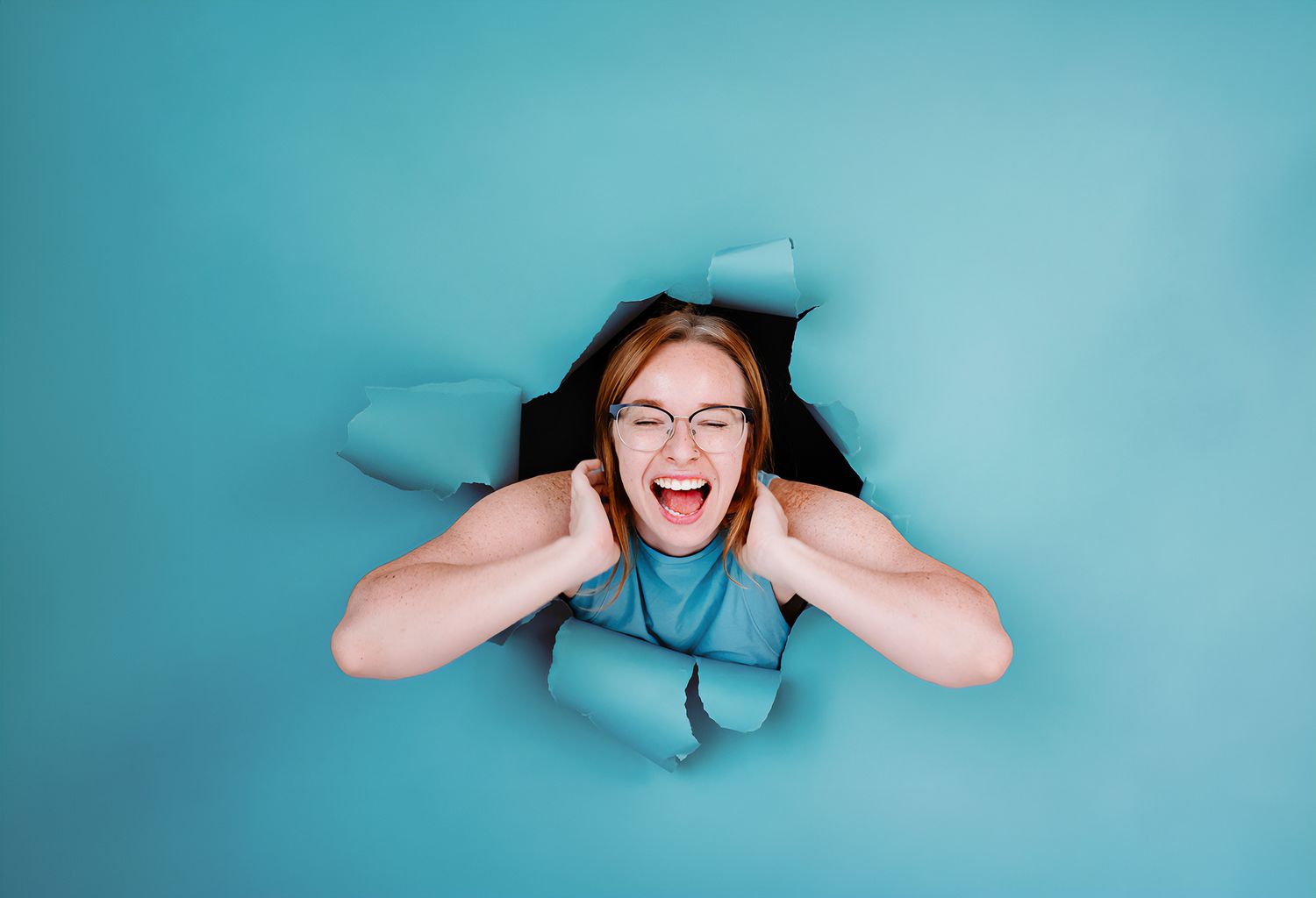 Playful portrait breaking through blue paper background with surprised expression.