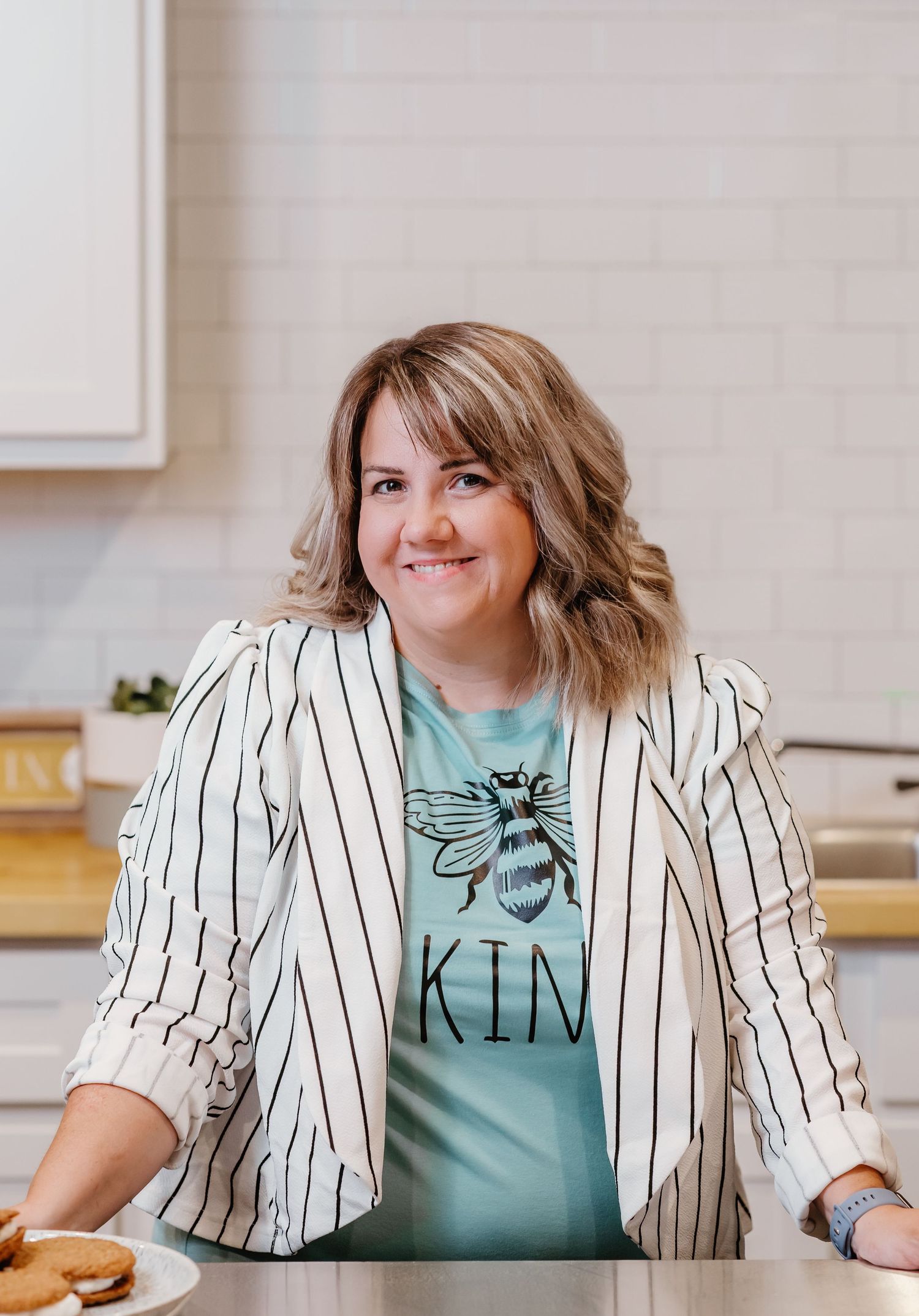 Professional wearing a striped blazer and mint green top sits at a desk with a bright smile.