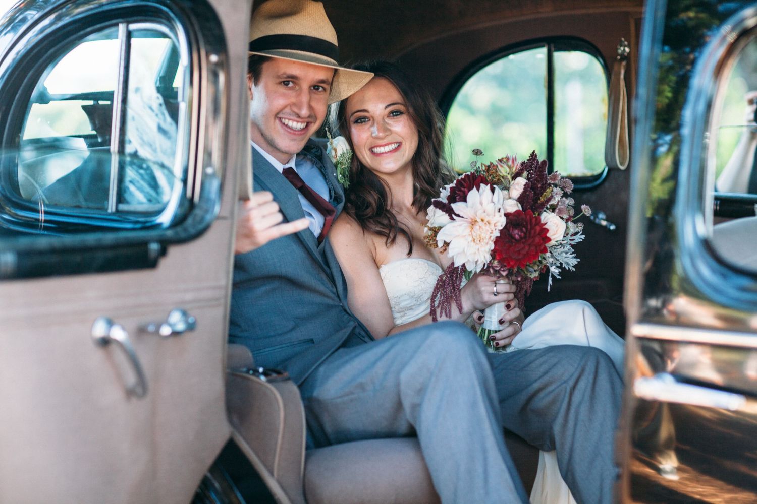 Just married! A joyful couple sitting inside a vintage car, dressed in classic wedding attire, radiating love and happiness