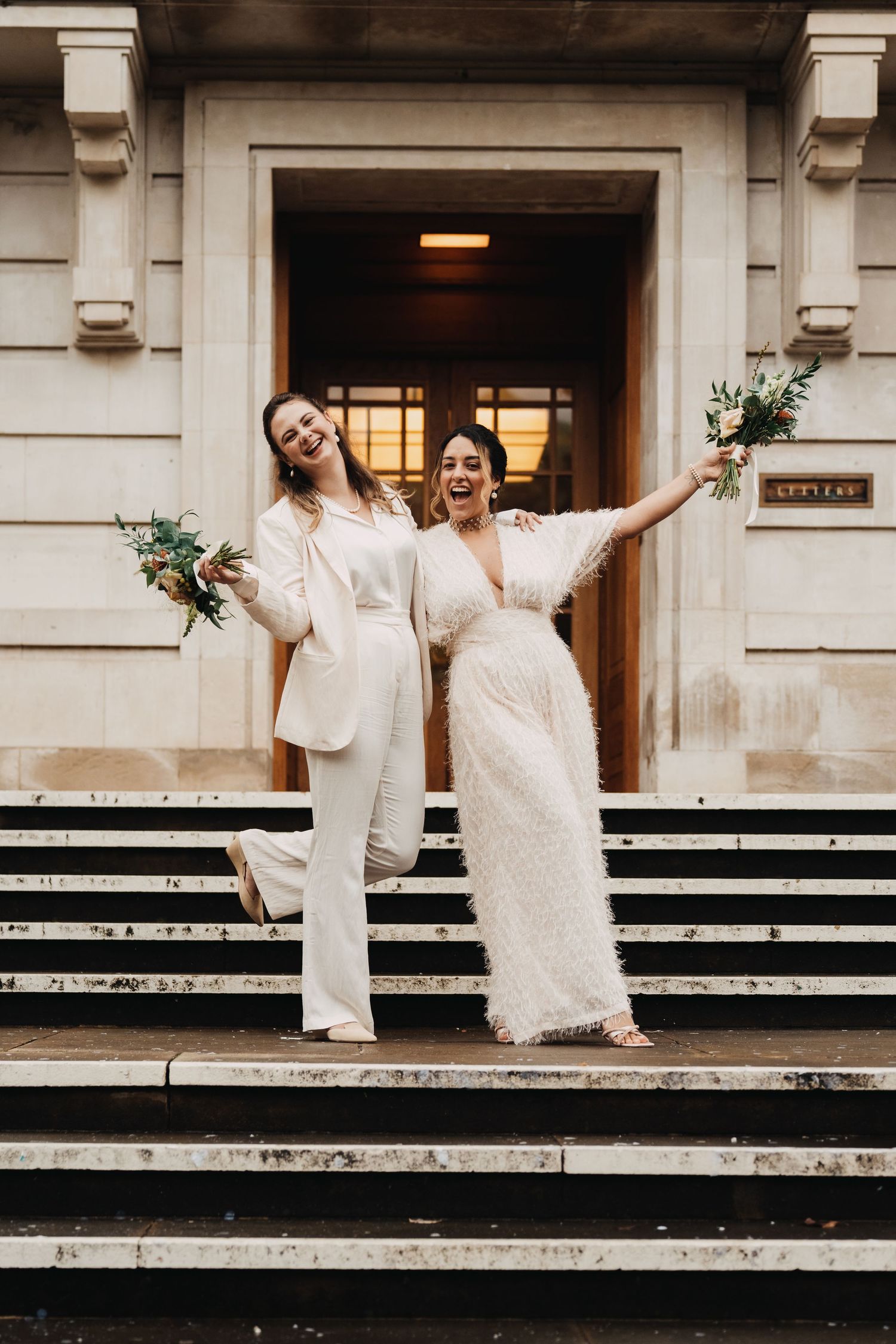 Two people in white outfits celebrate joyfully on stone building steps.