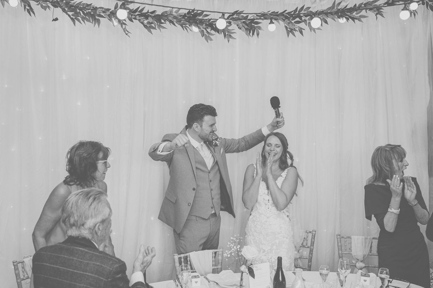 Wedding reception toast captured in black and white with evergreen garland decor.