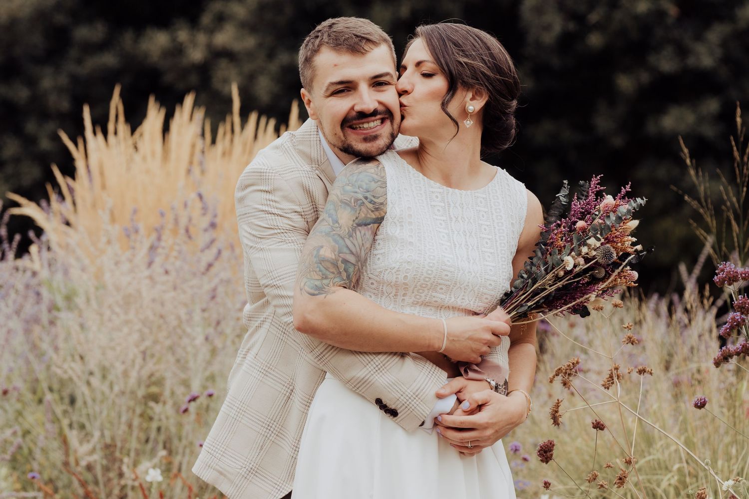 A couple embraces lovingly in a golden field of tall grass during sunset.