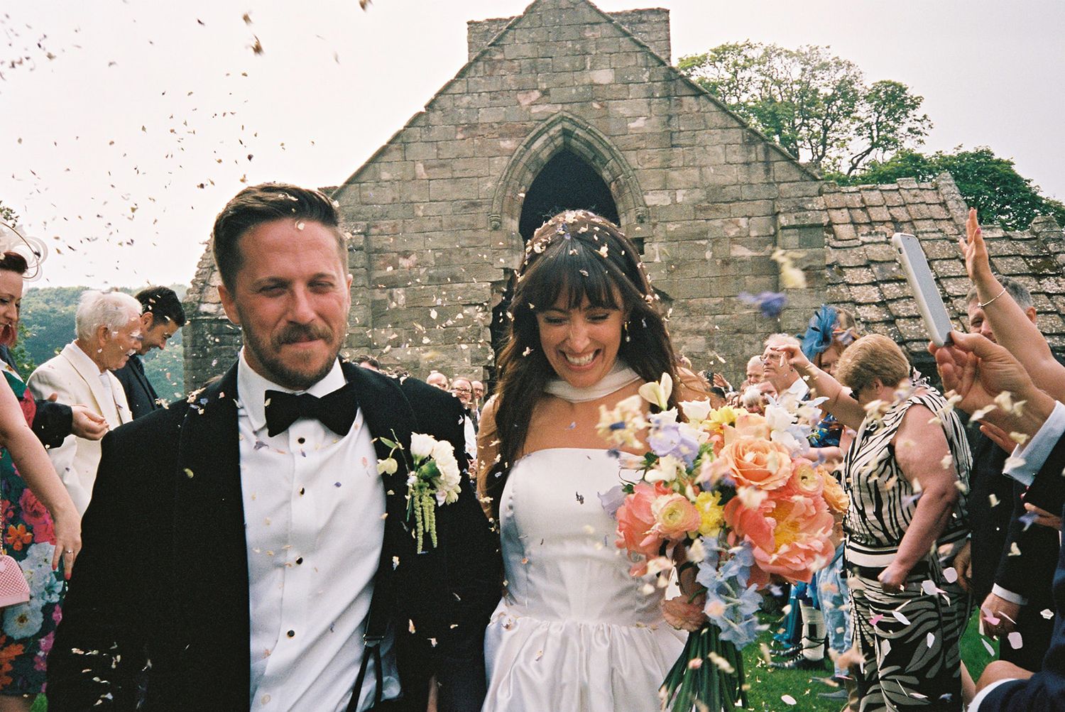 Newlyweds smiling and laughing as they are showered in confetti after their Scottish-Californian wedding ceremony at Dunglass Estate