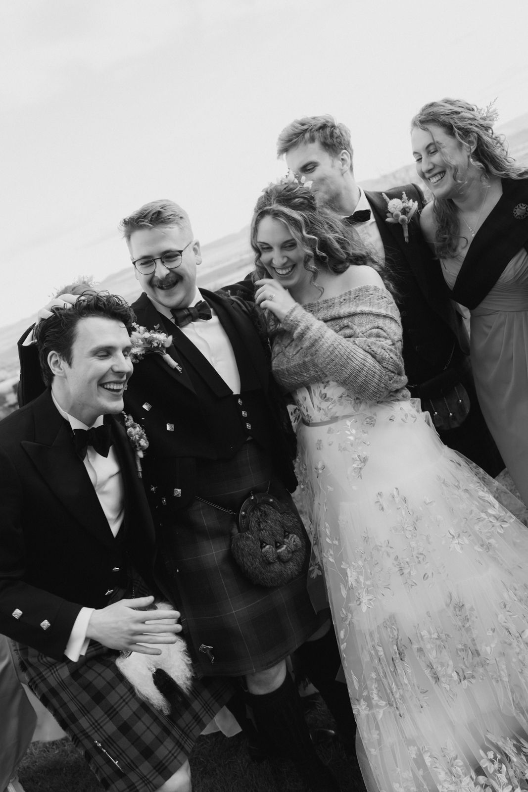 Informal black and white photograph of newlyweds laughing and celebrating with their wedding party at Guardswell Farm in Scotland