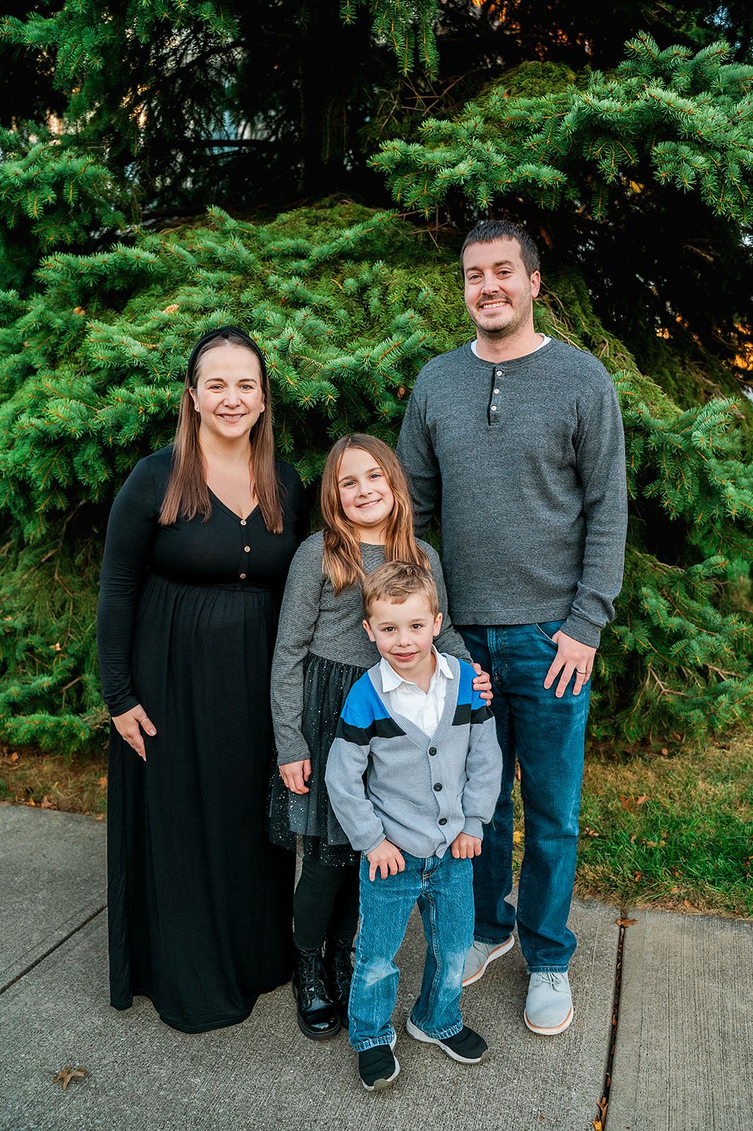 Family of four posing together against evergreen trees outdoors.