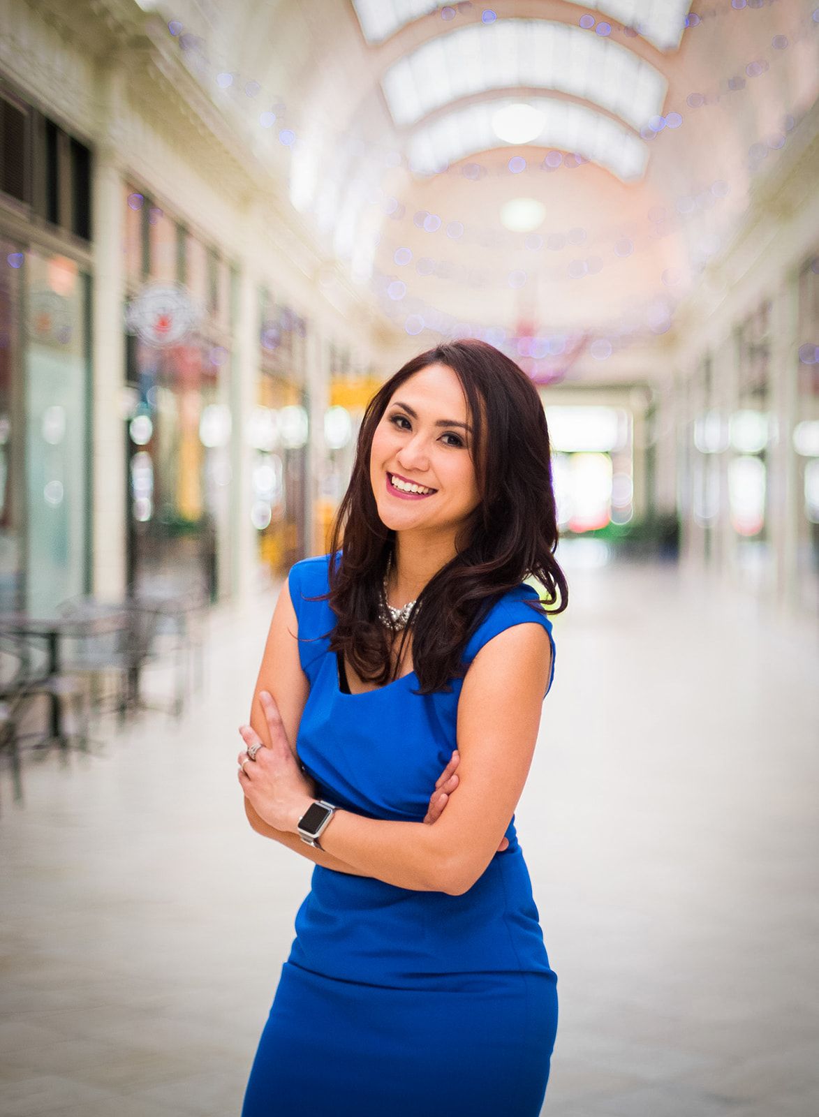Professional in blue dress standing confidently in elegant indoor shopping arcade.