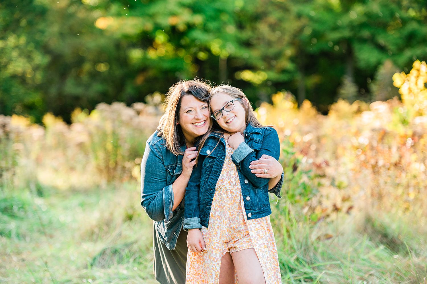 Mother and daughter embracing in casual denim outfits during golden hour outdoors.