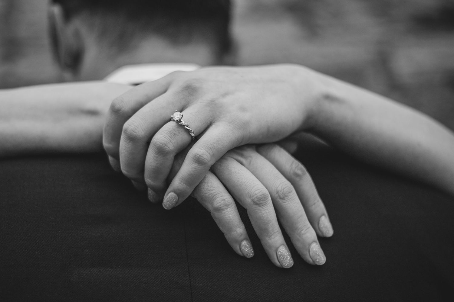Black and white close-up of hands with engagement ring showing tender moment.