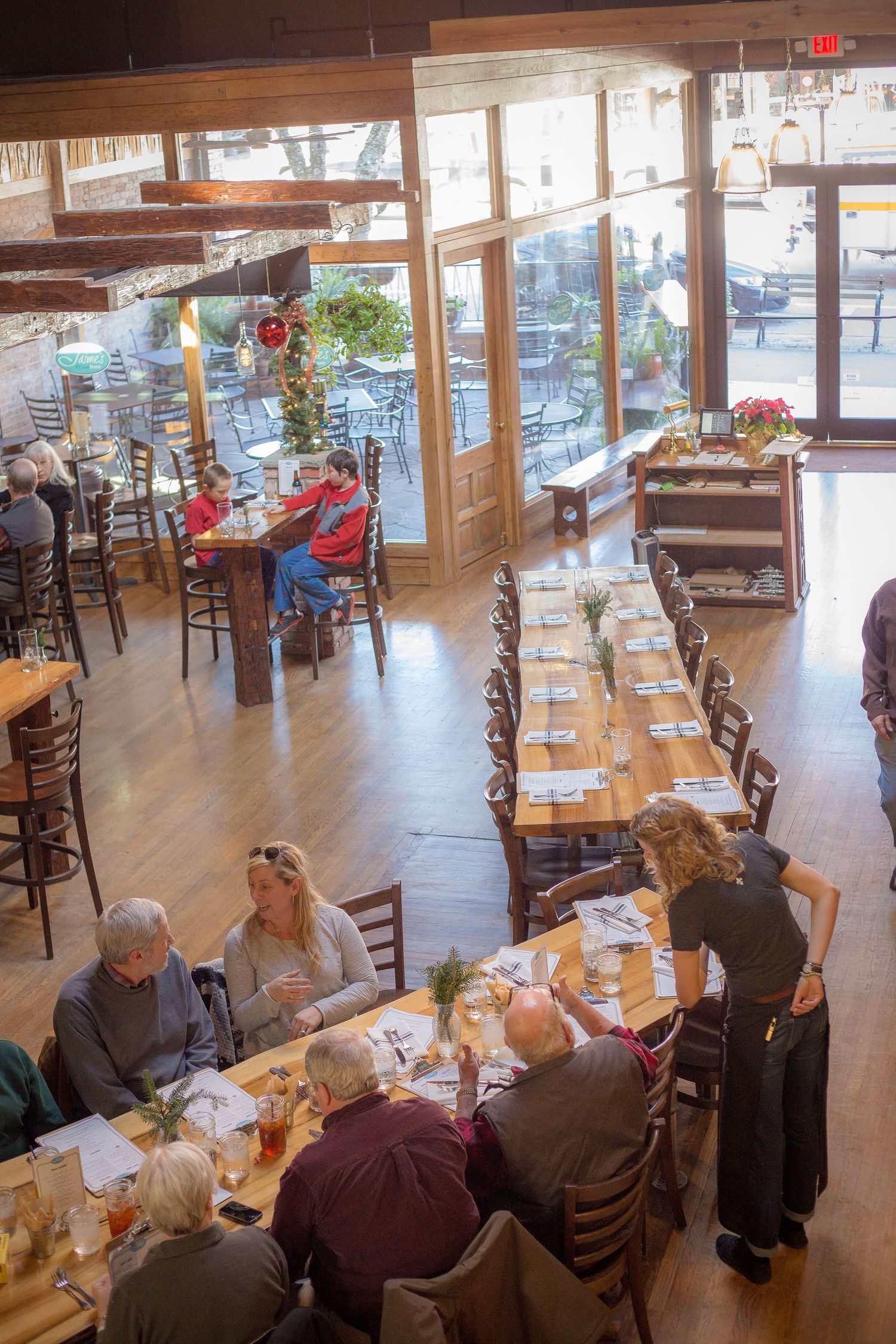 Busy restaurant interior with diners seated at long tables and large windows letting in natural light.