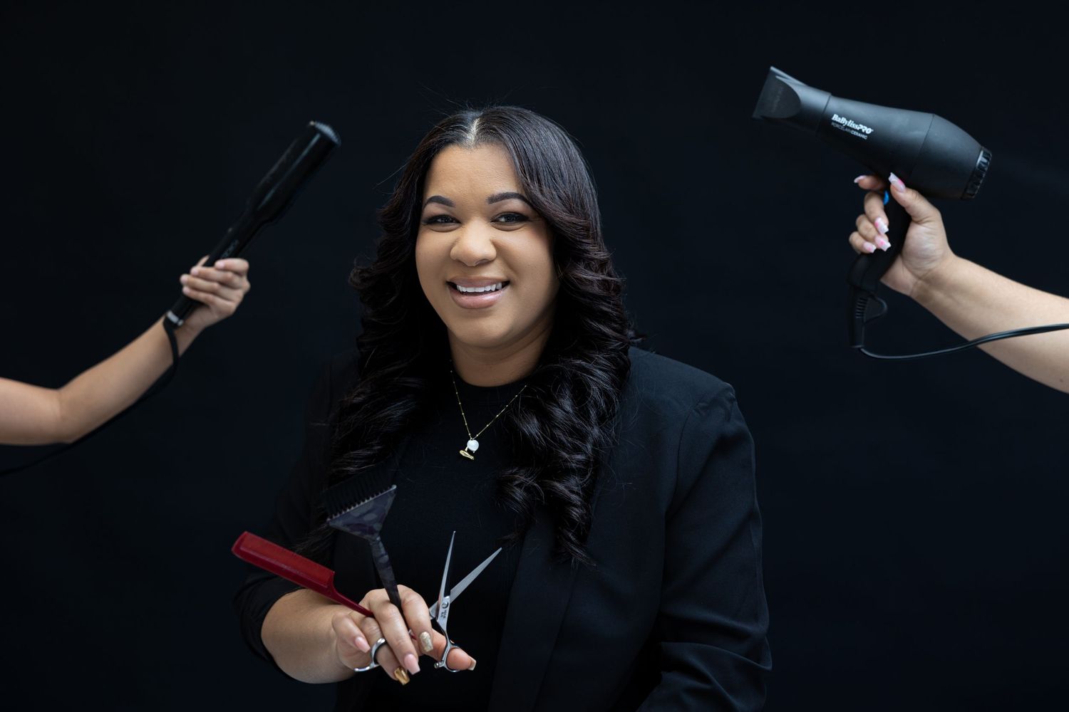 Hairstylist portrait with styling tools against dark background.