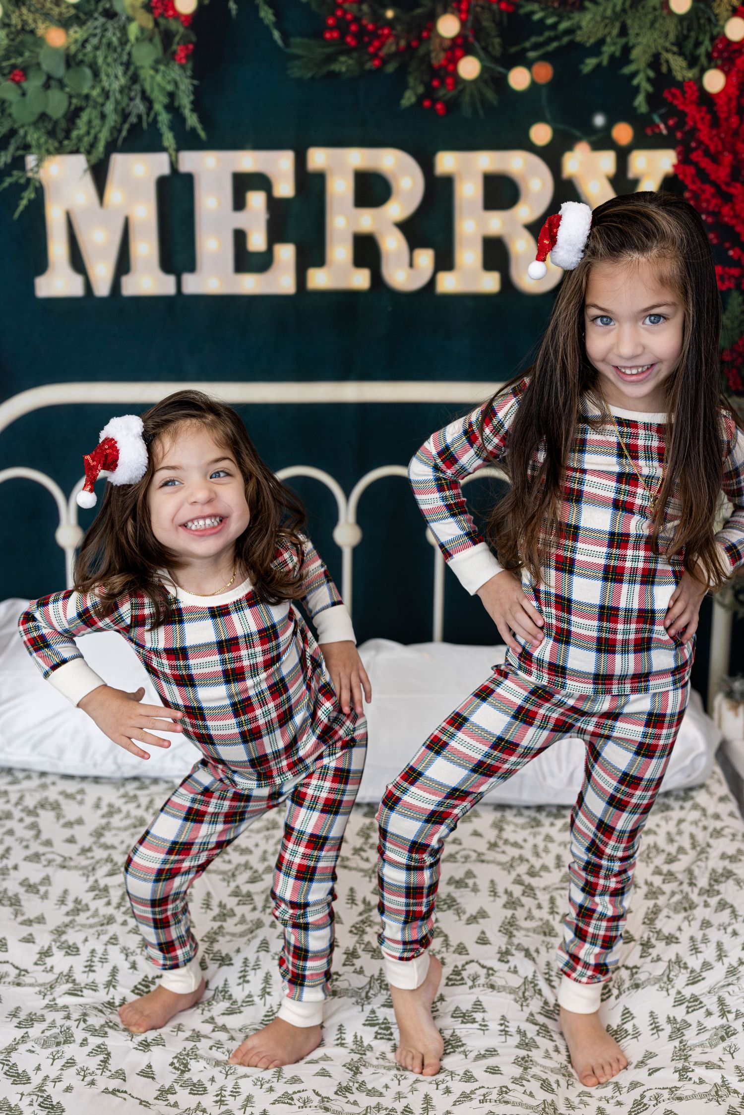 Sisters in matching plaid holiday pajamas pose in front of Christmas backdrop.