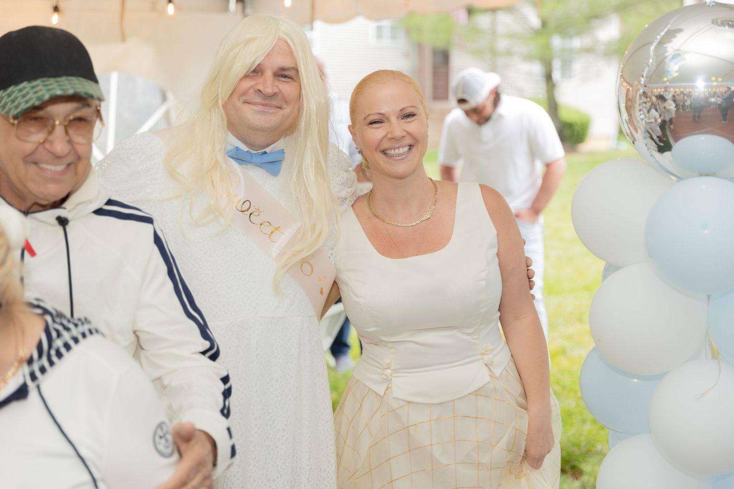 Wedding celebration with party goers in white outfits against light blue balloon decorations.
