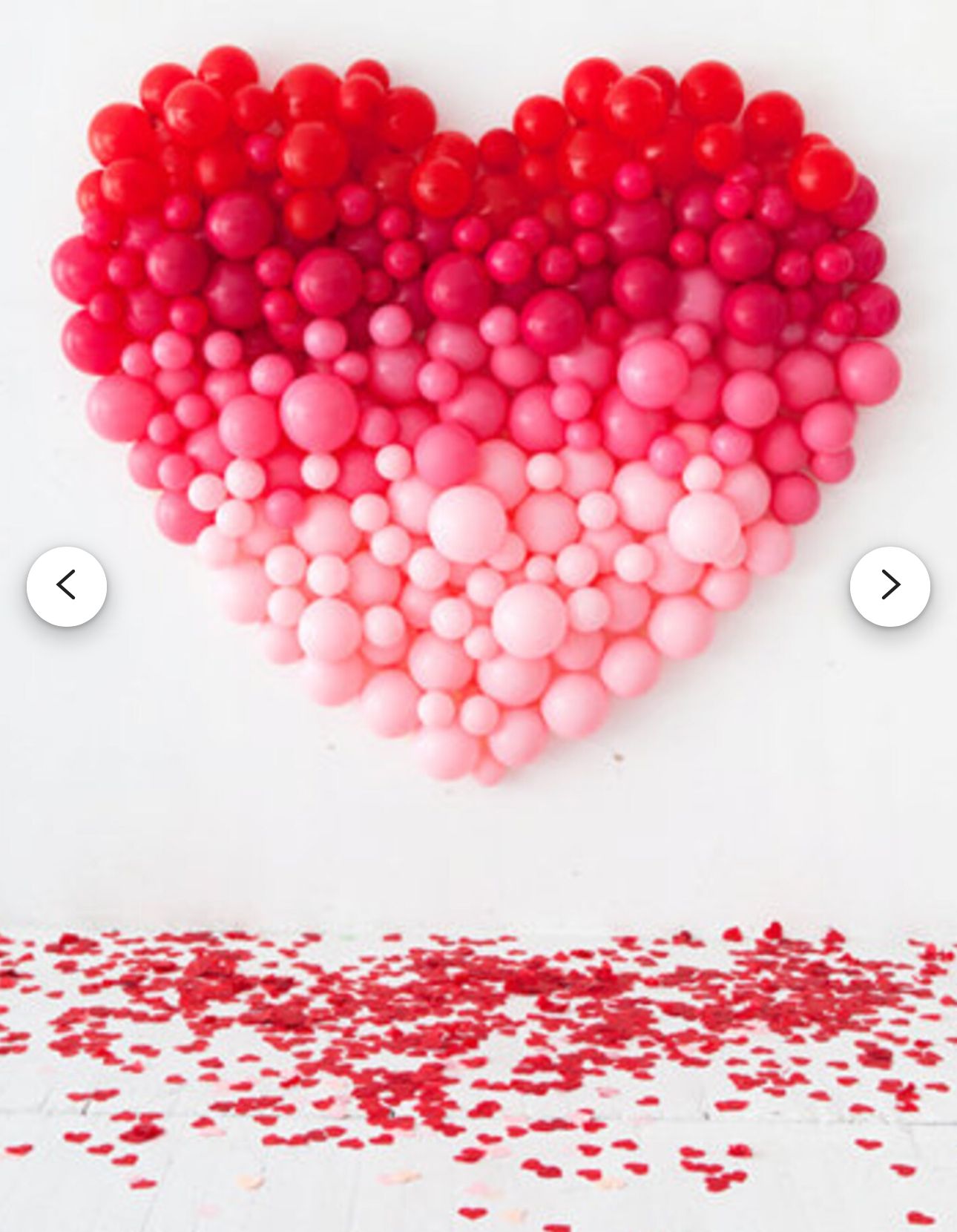 Ombre balloon heart wall decoration in red and pink shades with scattered petals below.