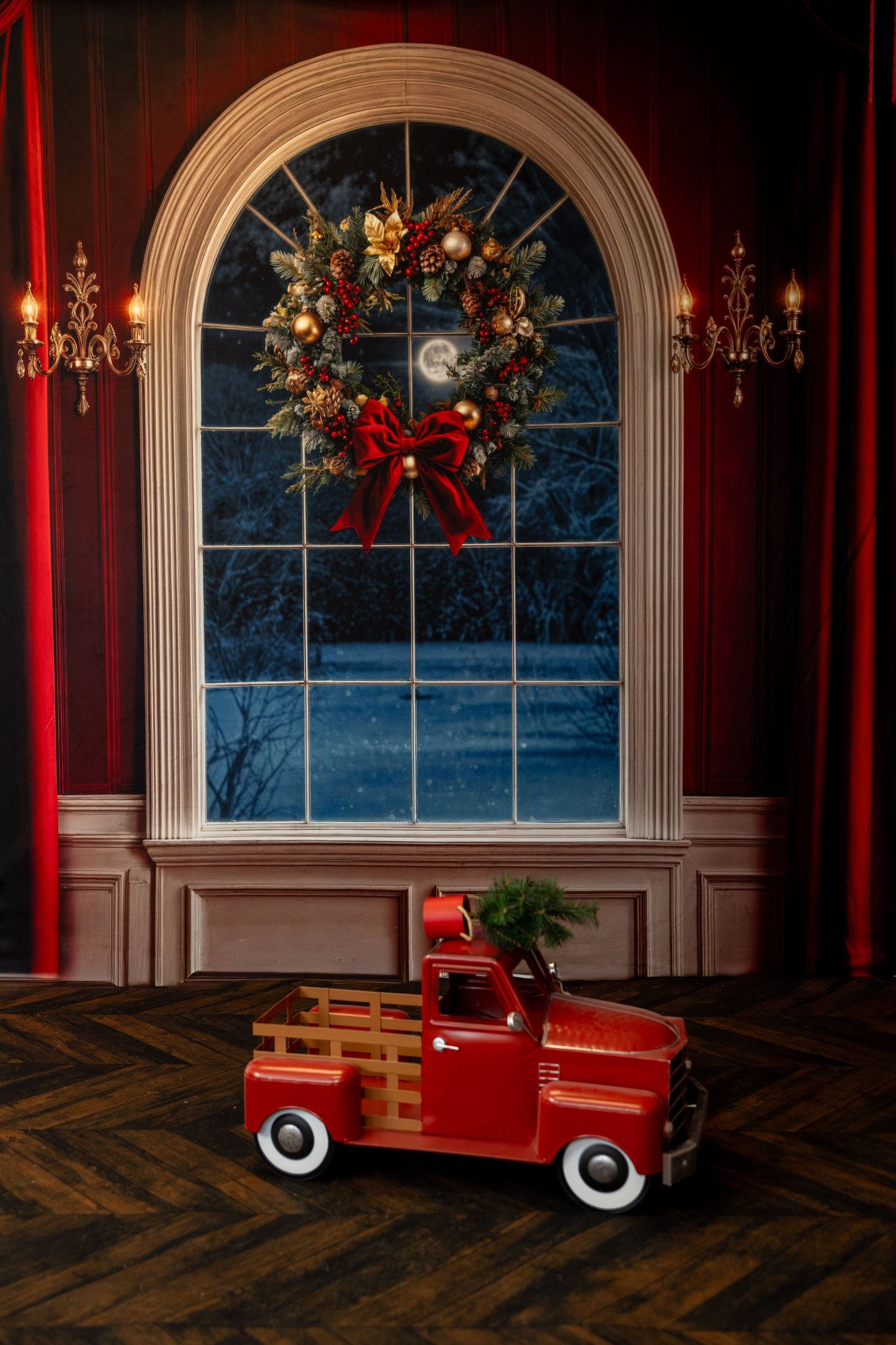Red vintage toy pedal car displayed in elegant room with arched window and holiday decorations against burgundy walls.