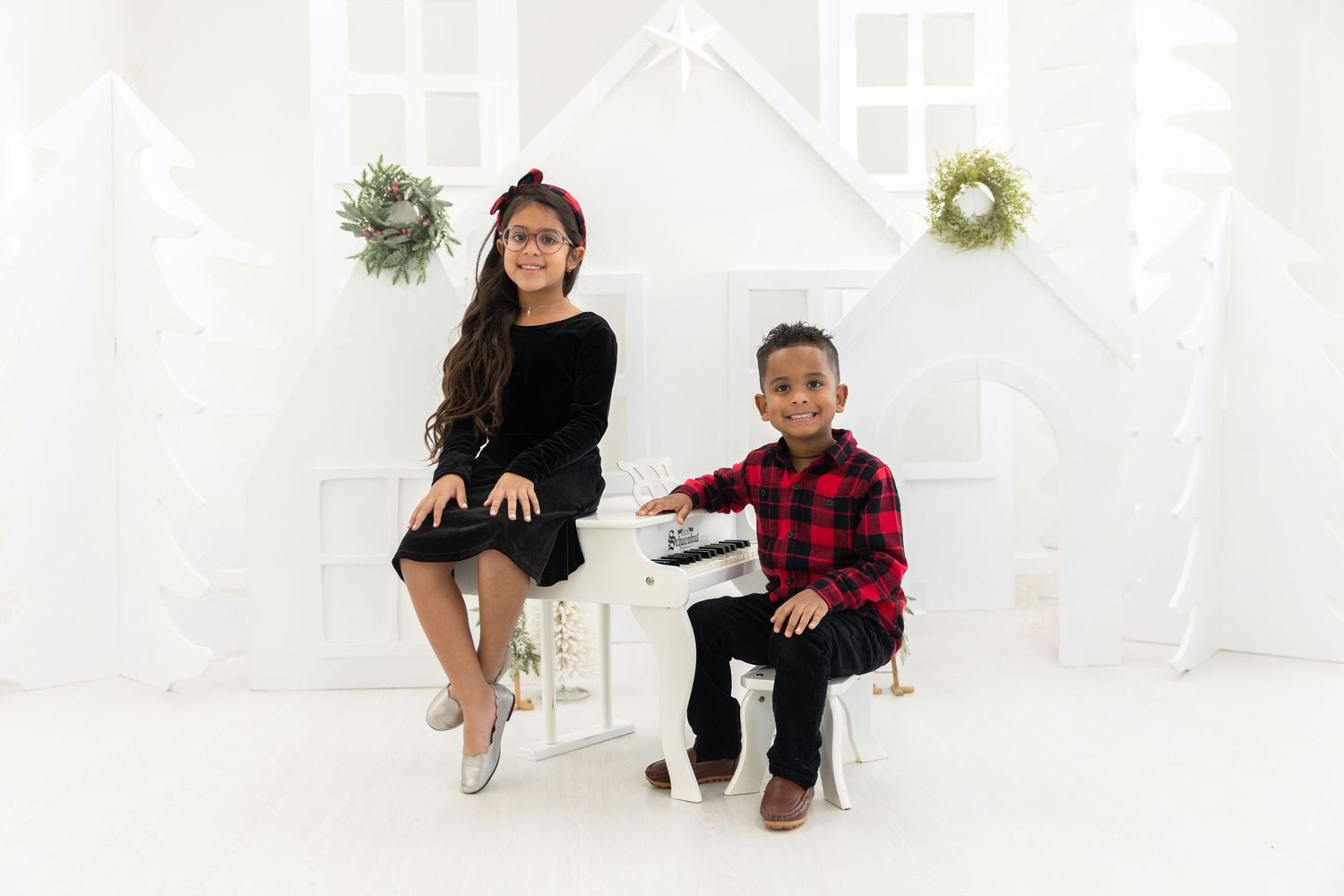 Two children sitting on rocking horses in front of white holiday backdrop with wreaths.